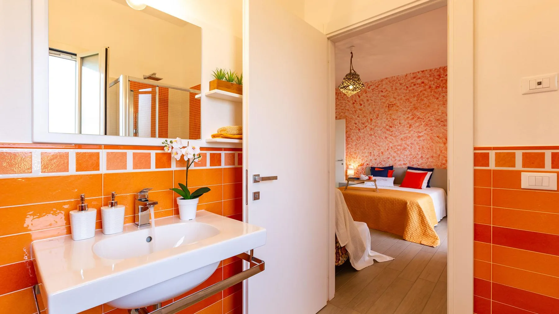 A bathroom vanity opens onto a bedroom with a bed and patterned wall.