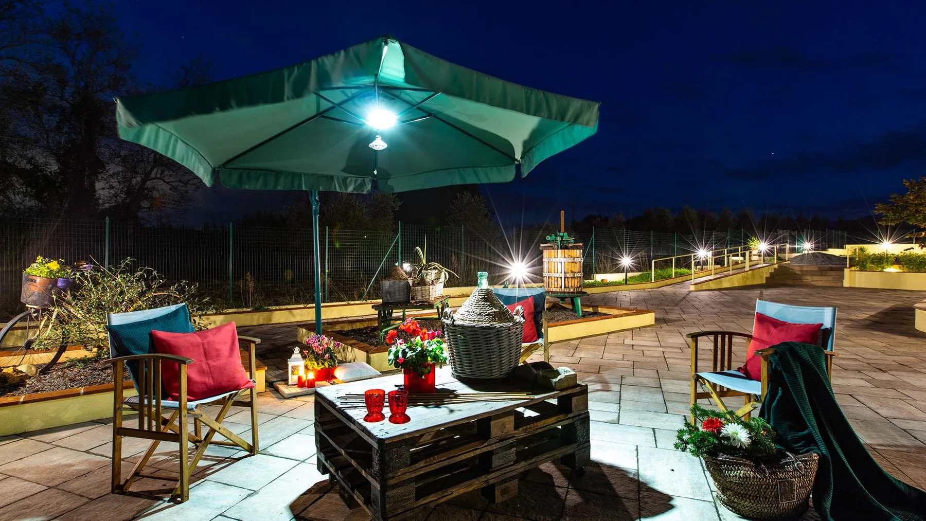 A paved outdoor patio at night with a large umbrella over a table.