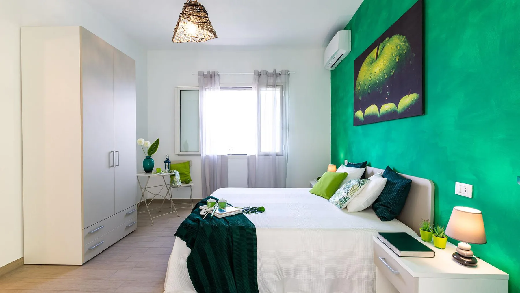 A bedroom with a bed beside a green accent wall and wardrobe.