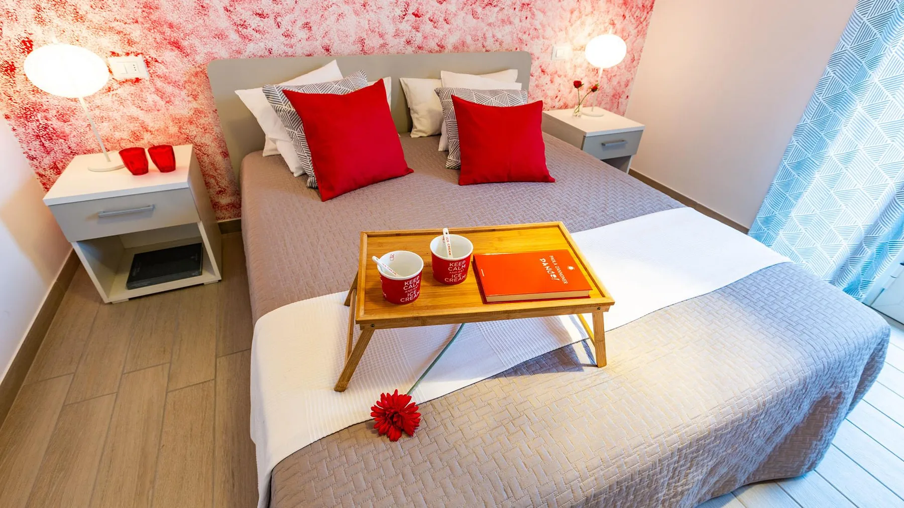 A bedroom with a bed dressed in gray bedding and red accent pillows.