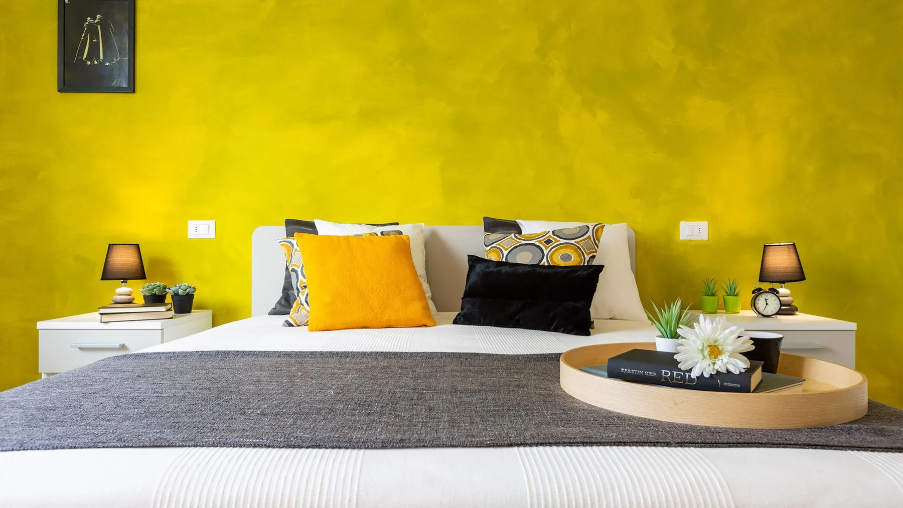 A bedroom with a bed arranged with colorful pillows and a gray throw.