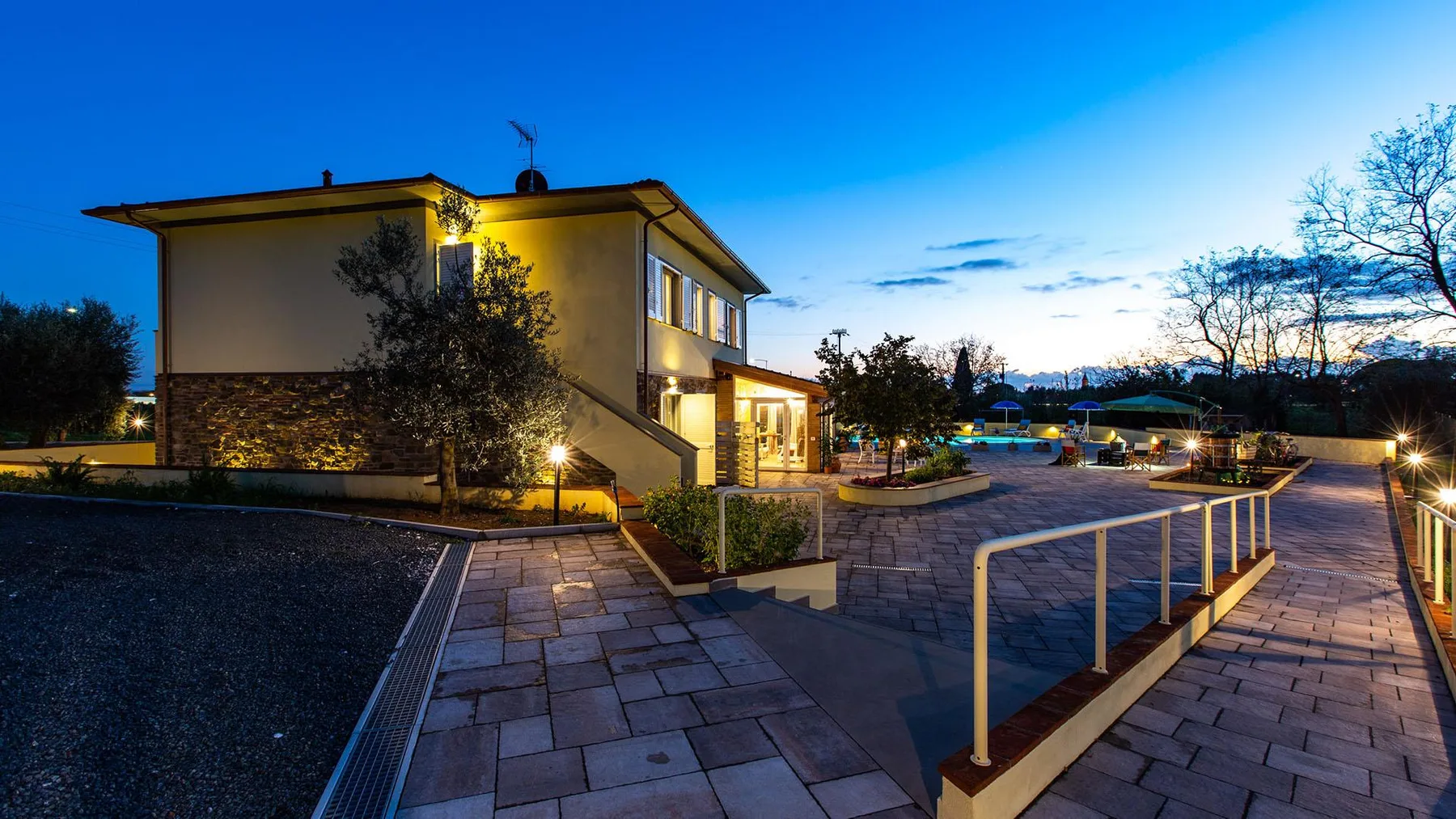 A modern building and paved walkway are illuminated at dusk.