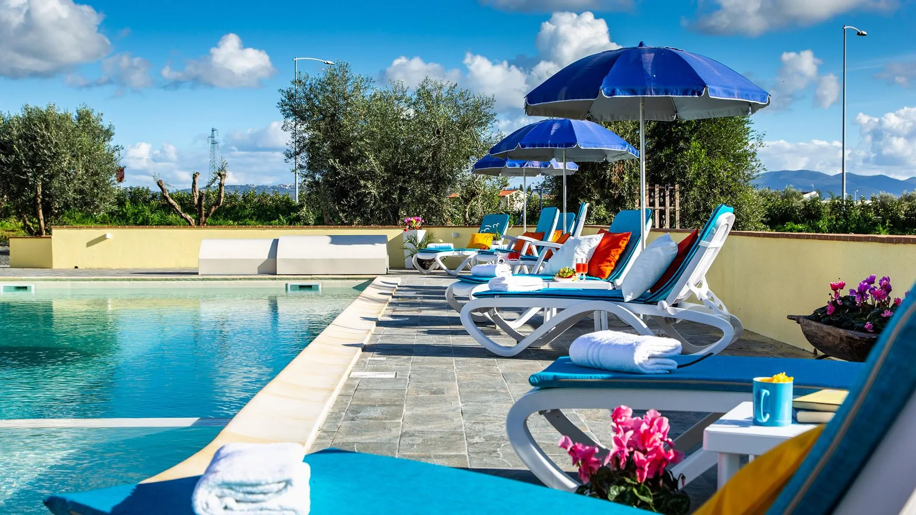 An outdoor swimming pool beside loungers under blue umbrellas.