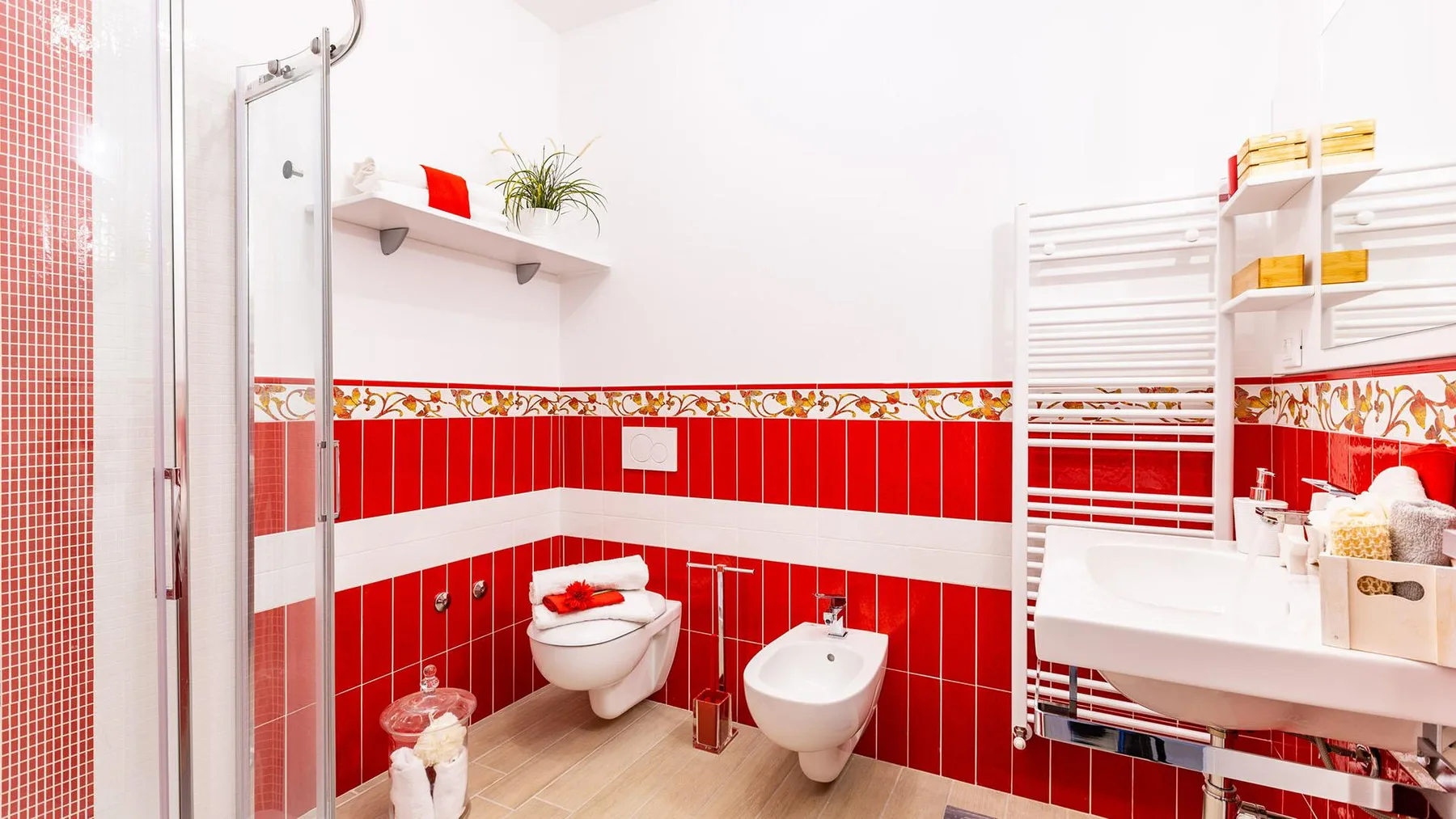 A bright bathroom with red tiled walls, a toilet, bidet, and sink.