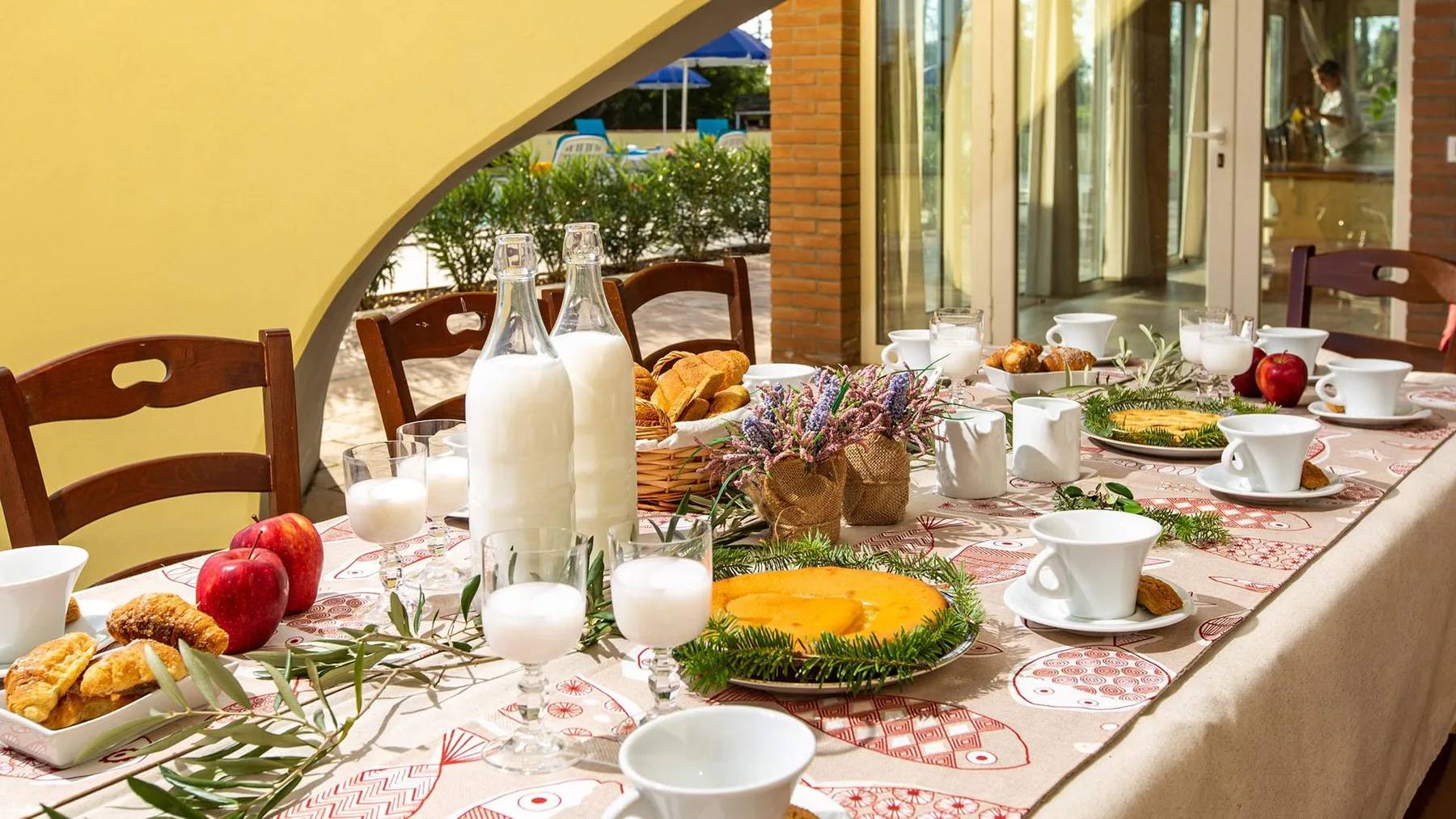 A breakfast table is set with pastries, fruit, drinks, and flowers.