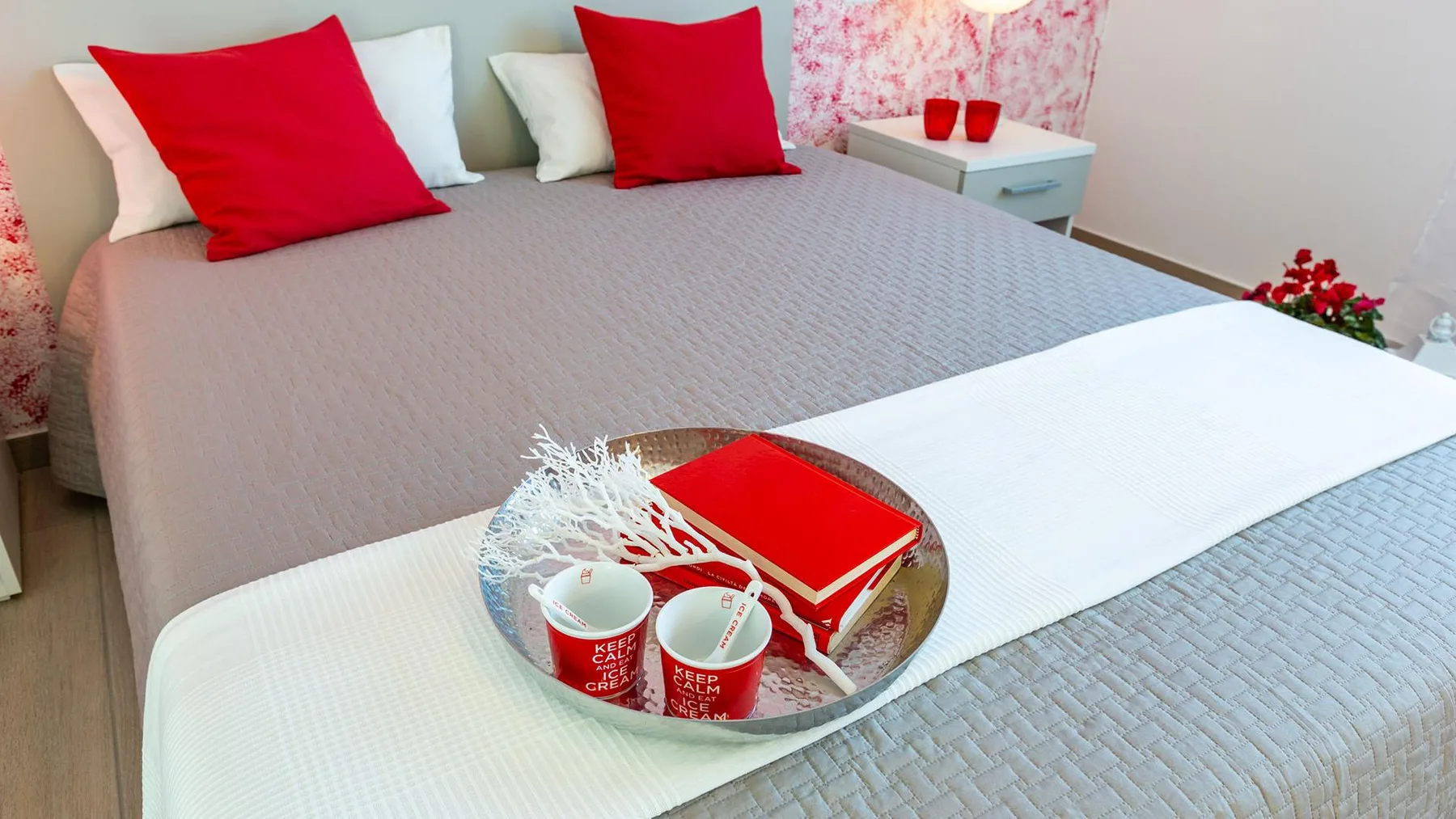 A neatly made bedroom bed has red pillows and a serving tray on the cover.