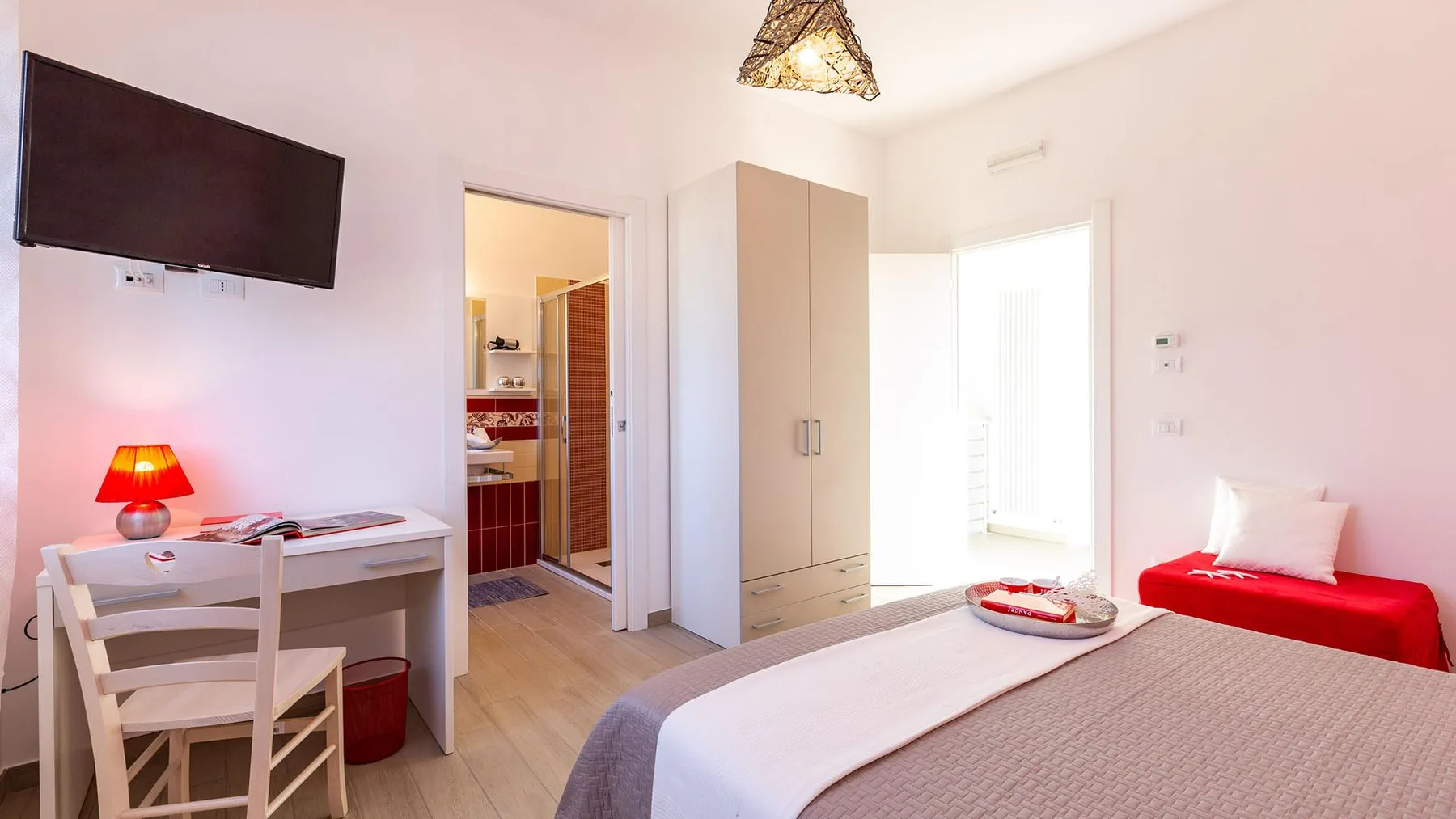 A bright bedroom with a made bed, a desk, and an open doorway to the bathroom.