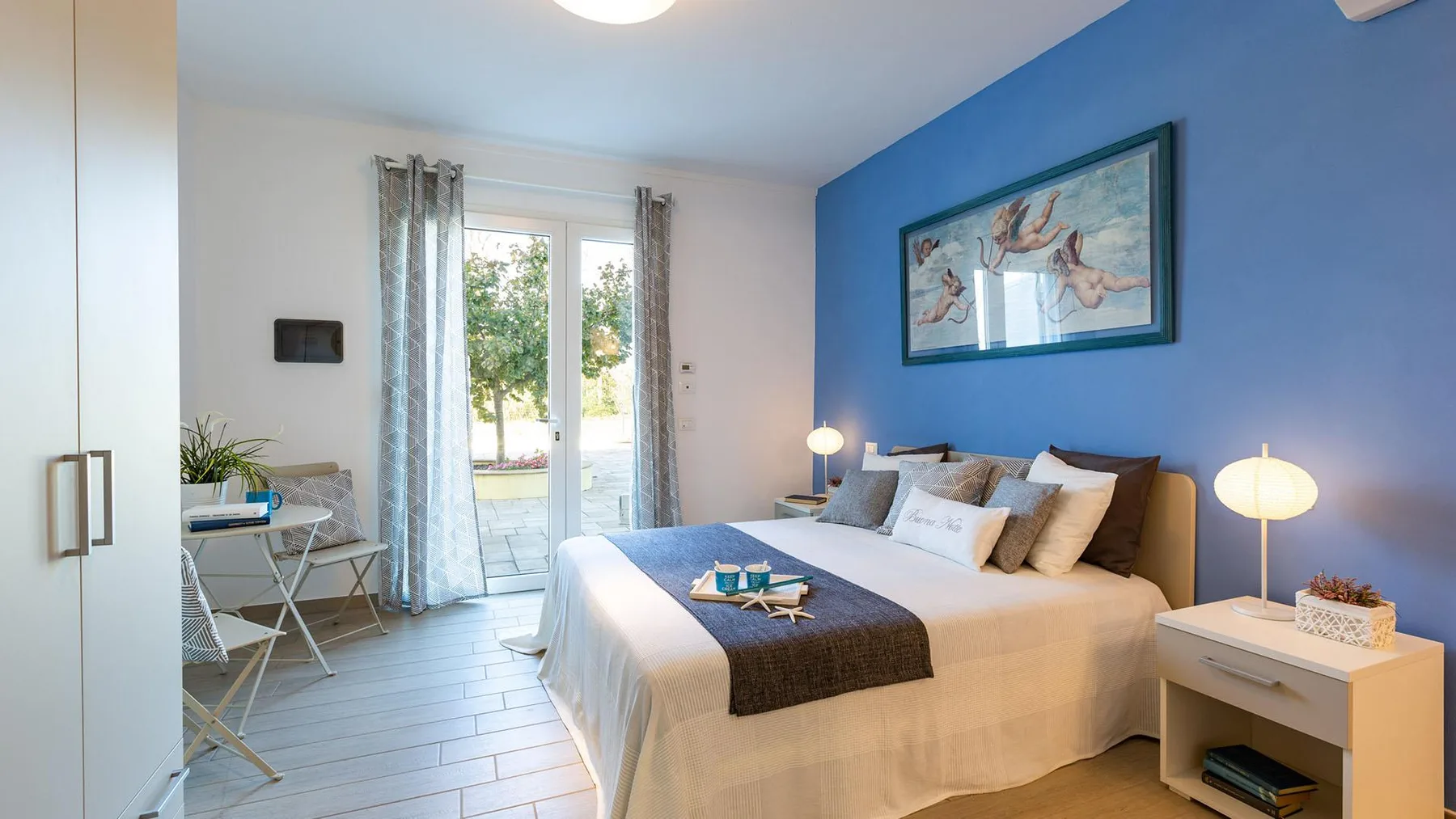 A bedroom with a double bed, blue accent wall, and glass doors opening to a patio.