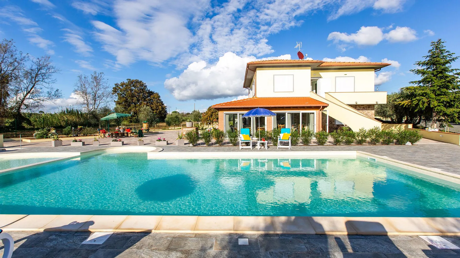 A swimming pool sits in front of a house under a partly cloudy sky.