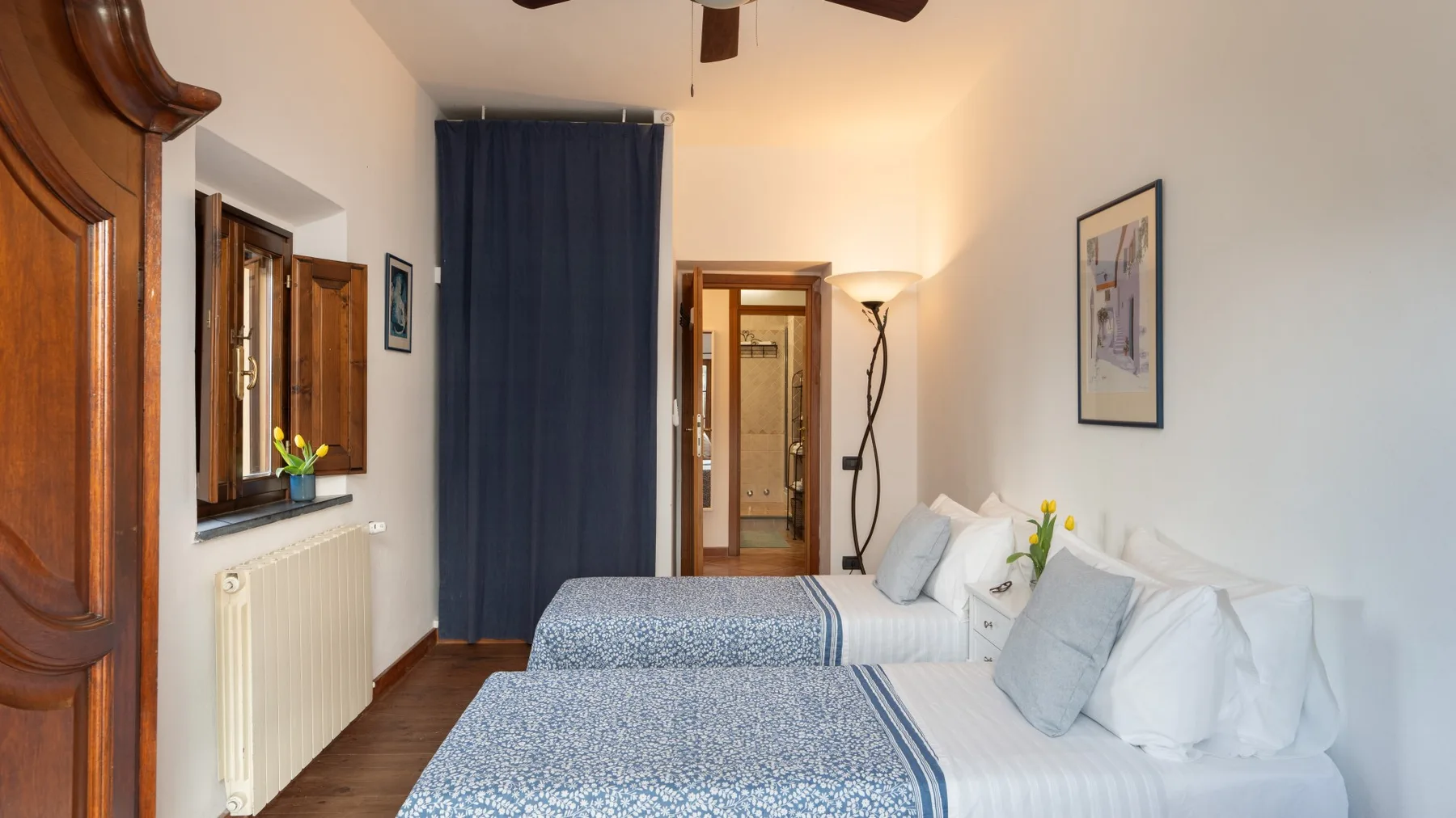 Un dormitorio con dos camas vestidas con ropa de cama azul y blanca junto a una cortina oscura.