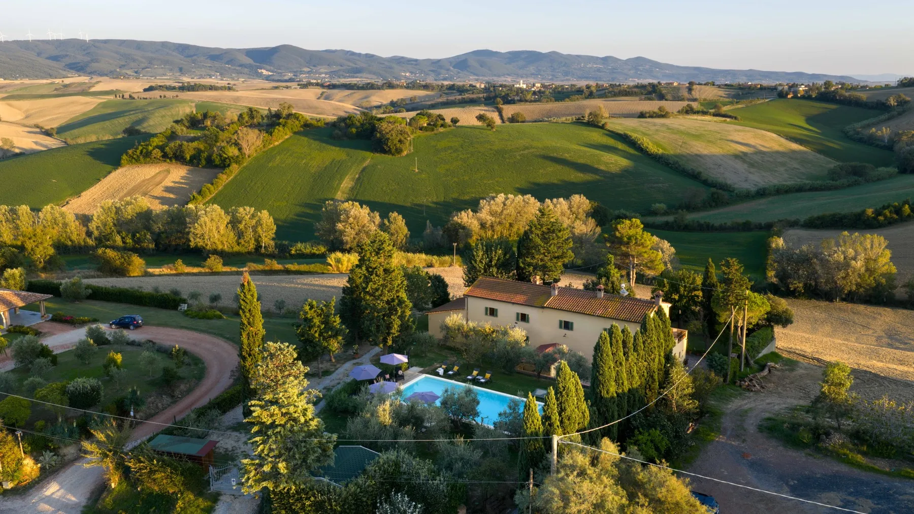 Un paisaje rural de campos ondulados rodea una casa de campo y una piscina.