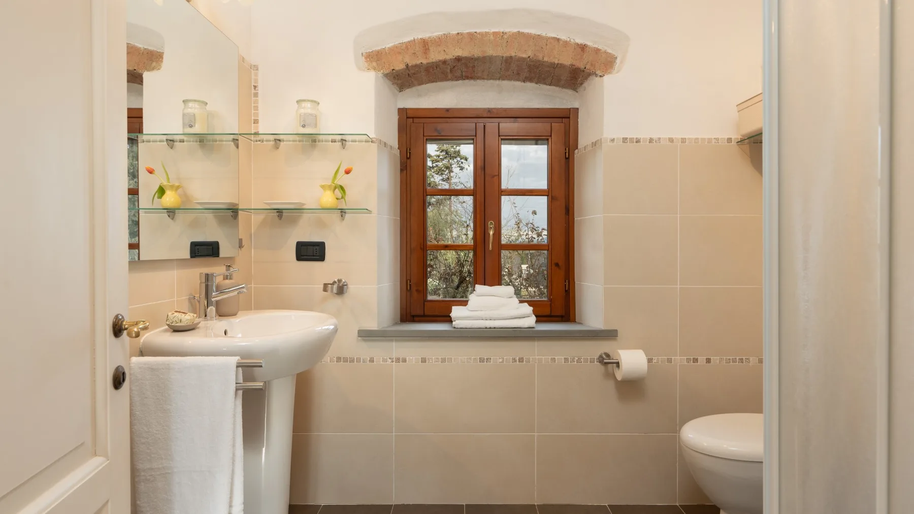 Un baño alicatado con lavabo de pedestal, ventana e inodoro.