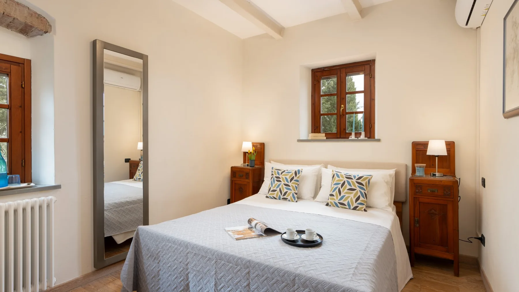 Un dormitorio con una cama, mesitas de madera y ventanas.