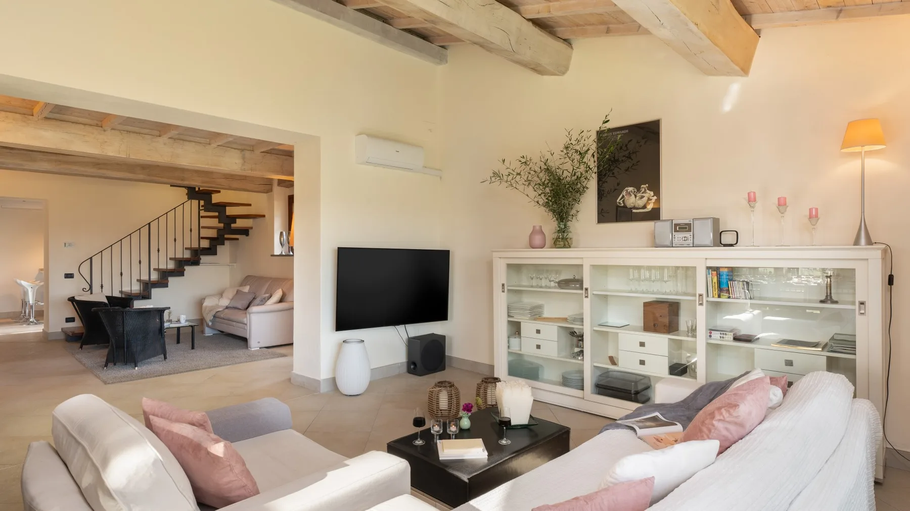 Una sala de estar luminosa con asientos claros, un televisor y estanterías abiertas.
