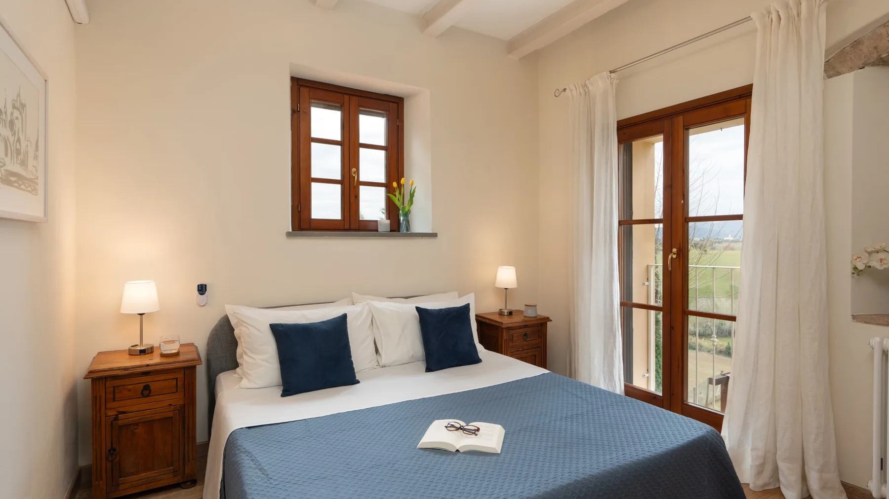 Un dormitorio con una cama bien tendida y ventanas de marco de madera que dan a un balcón.
