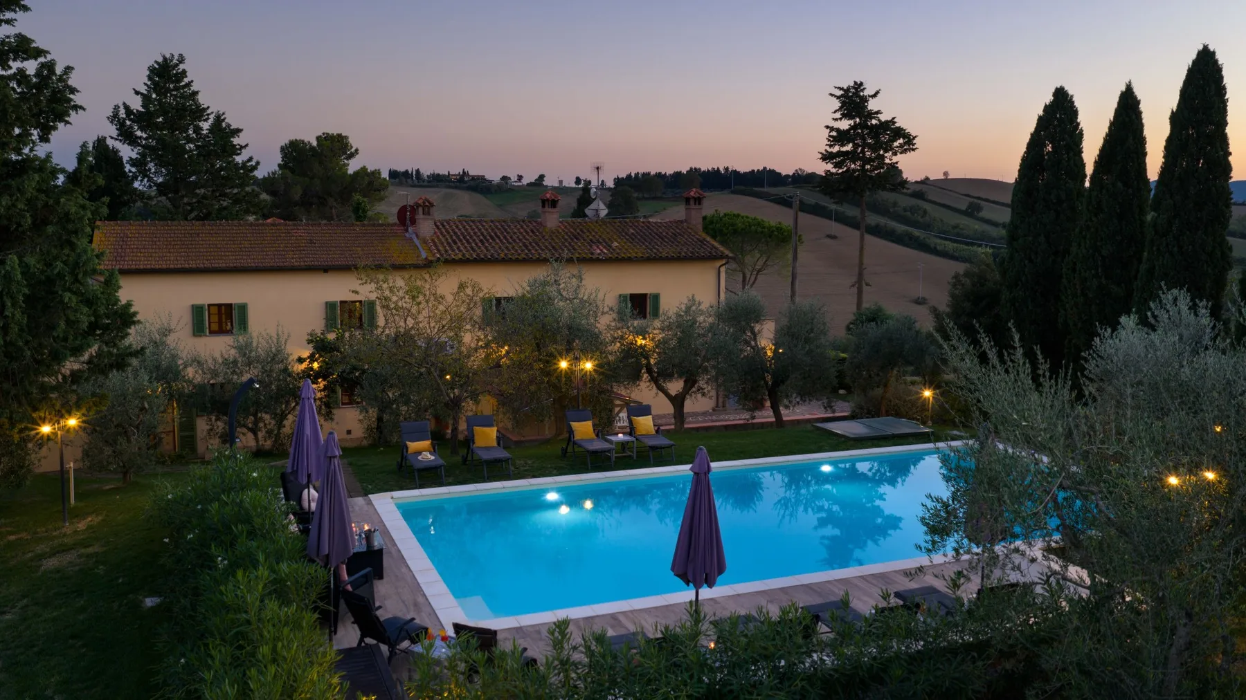Una piscina junto a un jardín y un edificio bajo al atardecer.