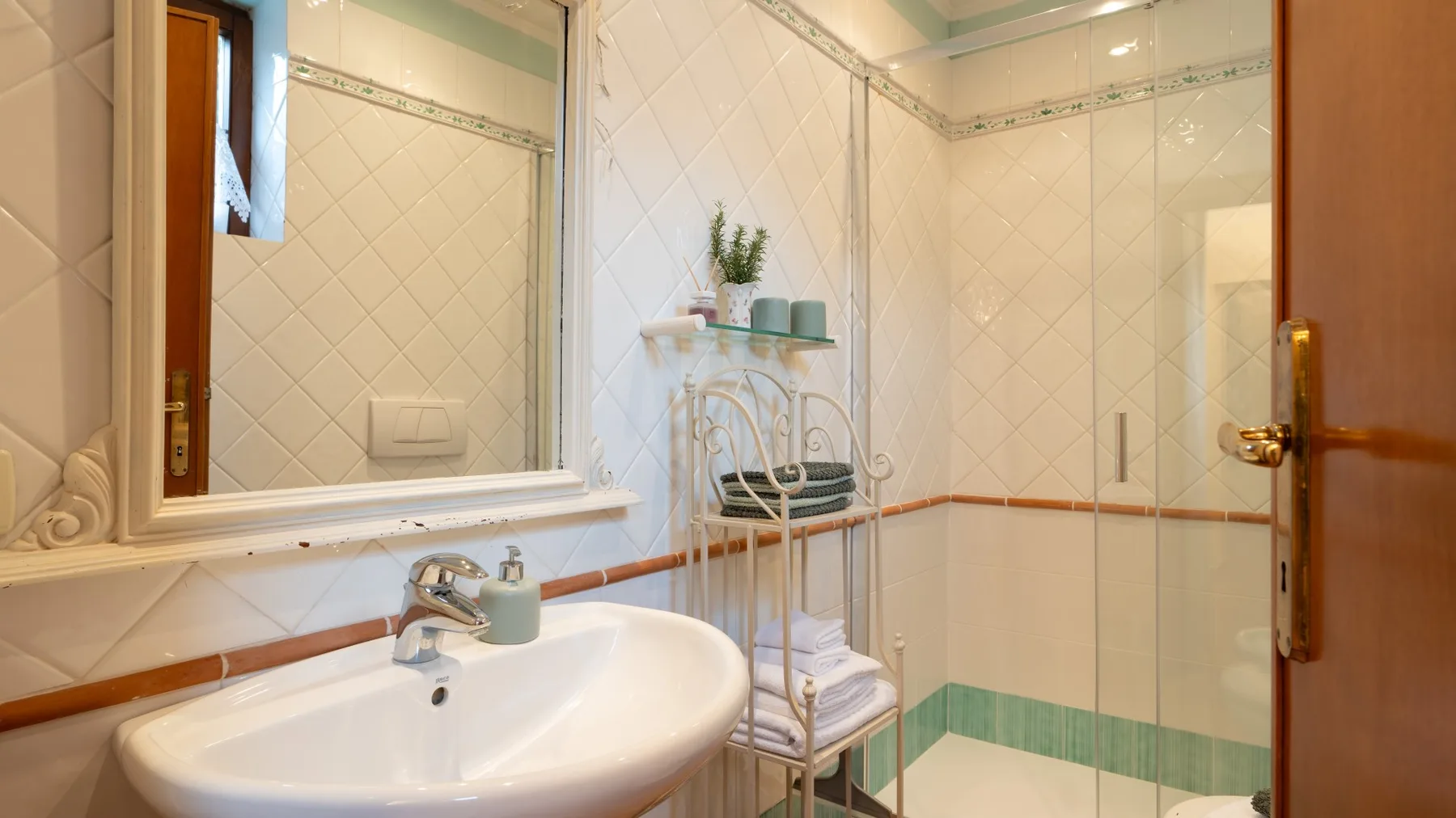 Un baño alicatado con lavabo, espejo y ducha de vidrio.