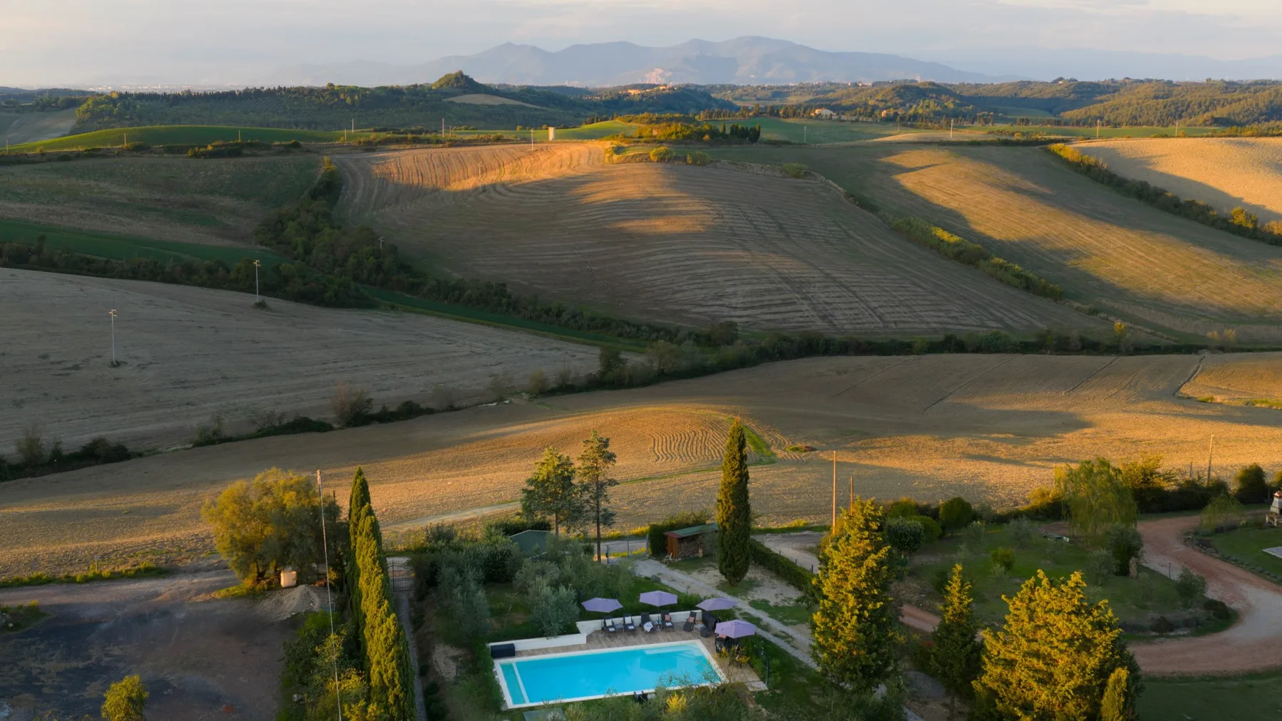 Paisaje rural de campos ondulados, con una piscina entre árboles en primer plano.