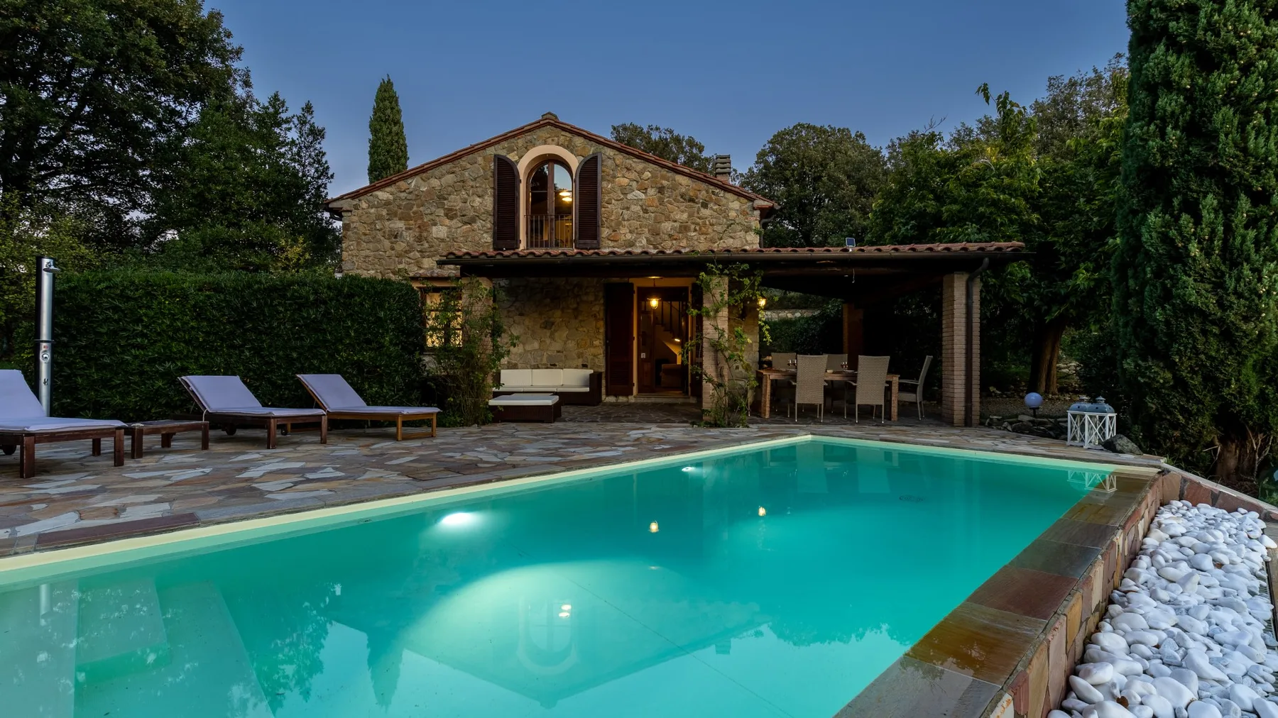 Una piscina al aire libre está junto a un edificio de piedra y un patio cubierto.
