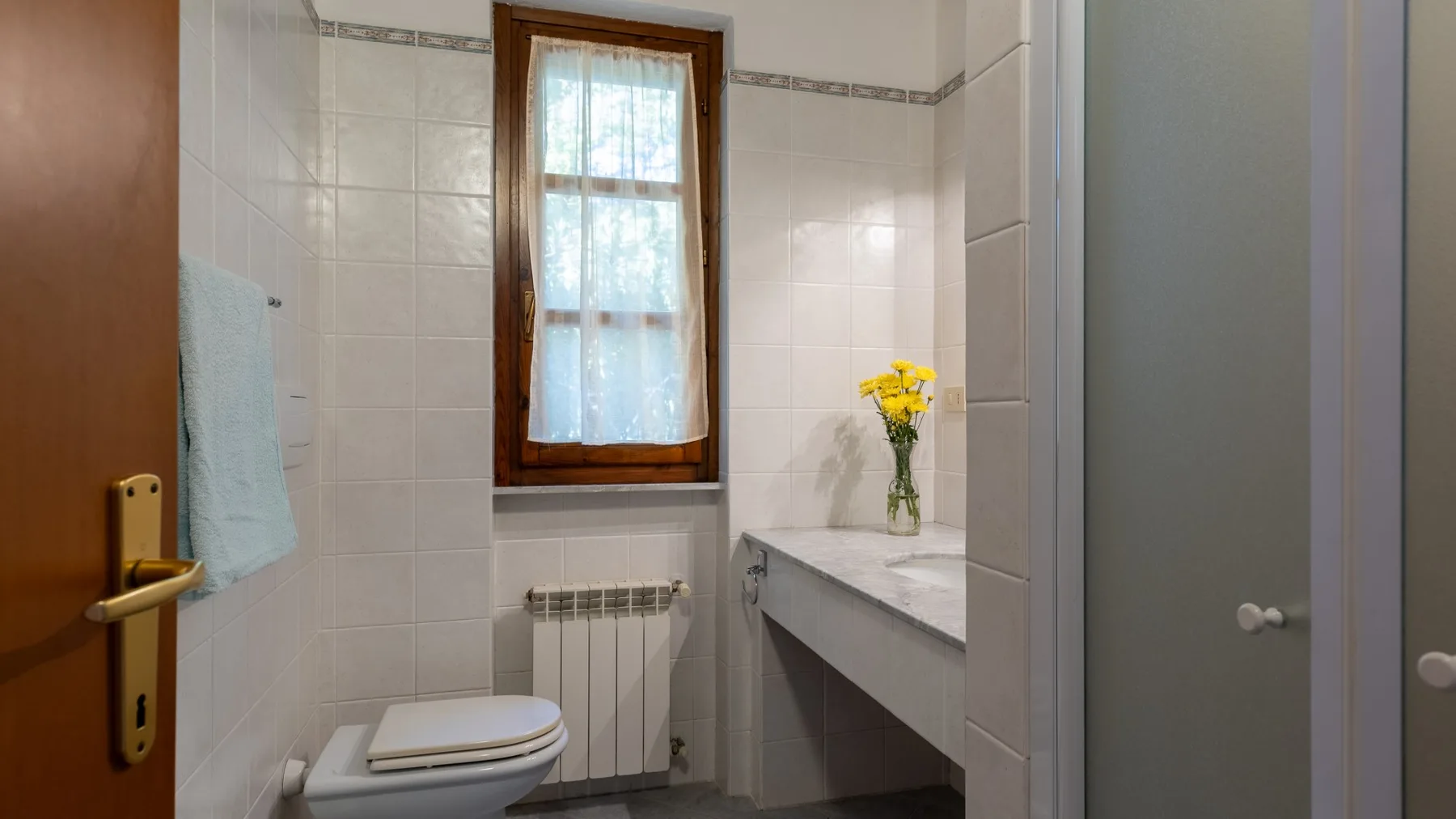 Un baño alicatado con inodoro, lavabo y ventana.