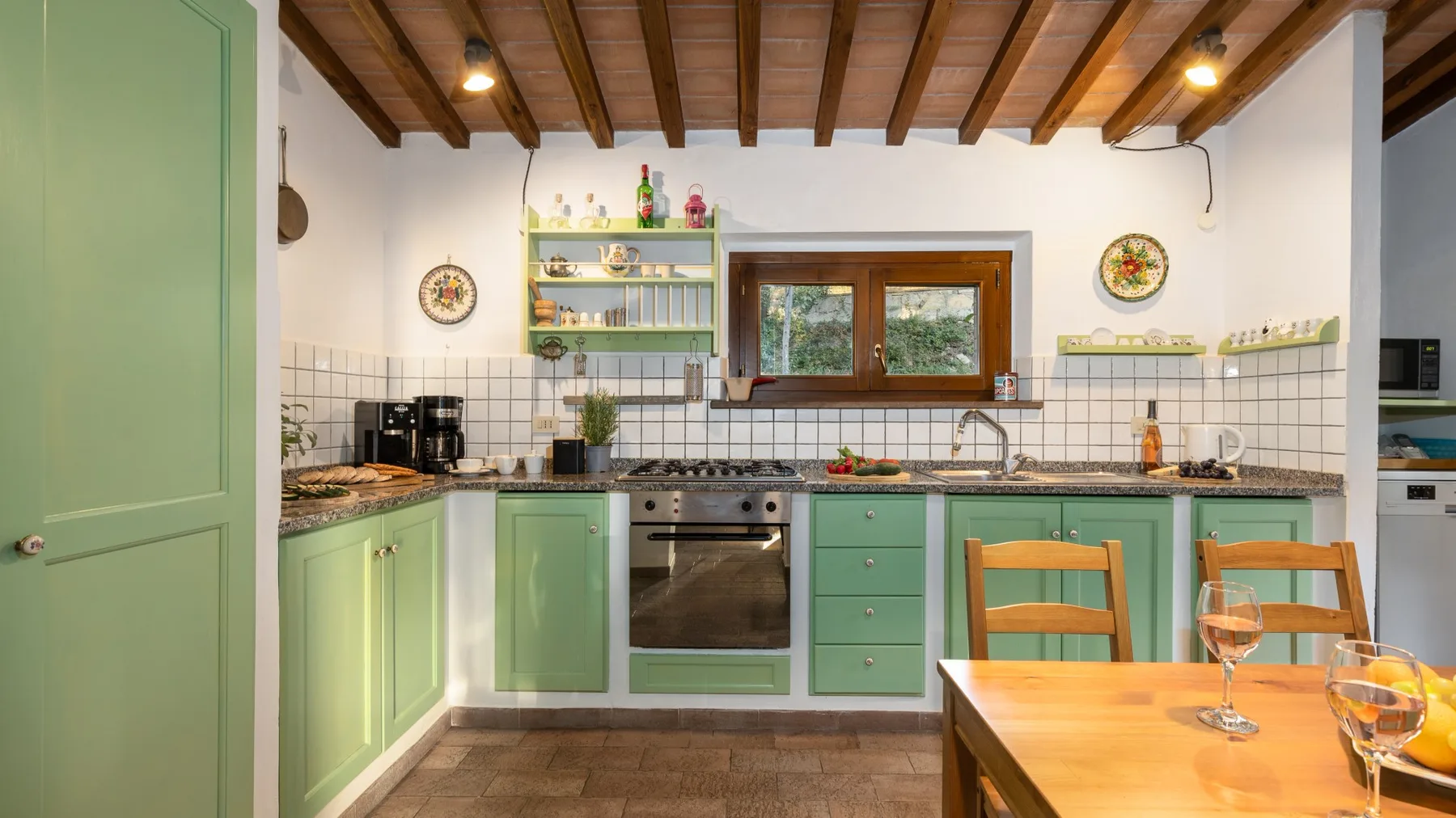 Una cocina verde con una mesa de comedor de madera y vigas de techo a la vista.