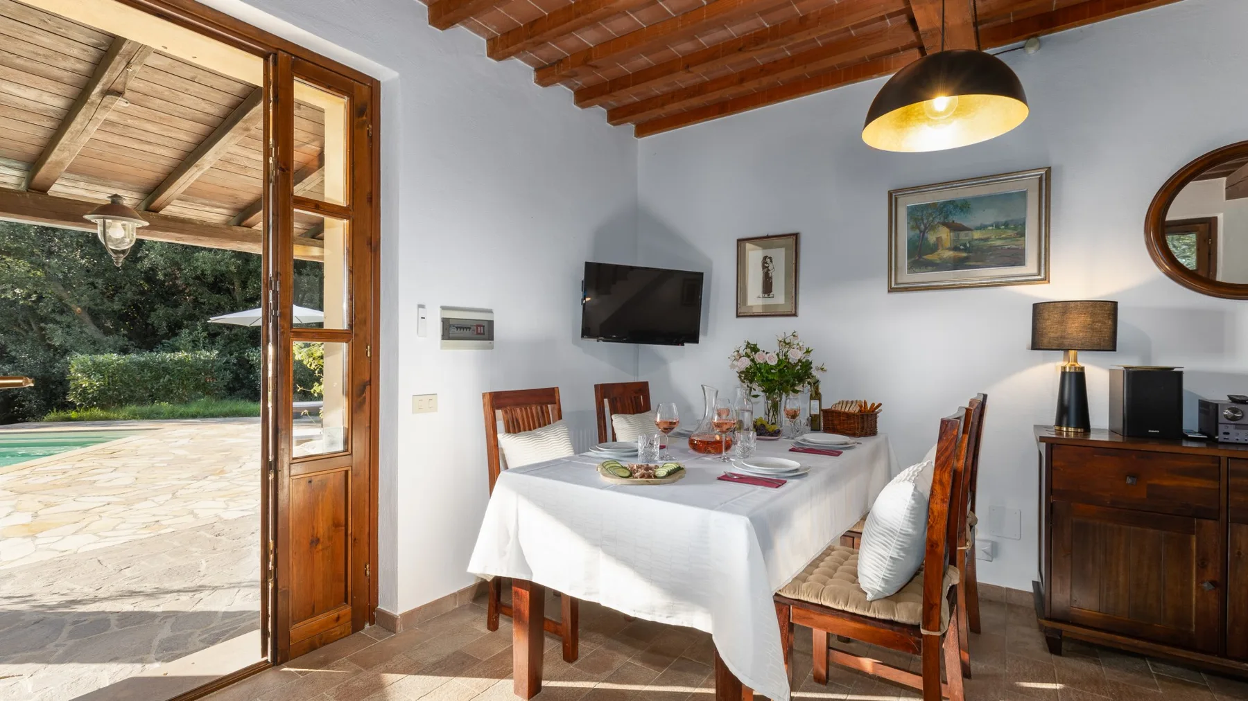 Un comedor con una mesa puesta junto a puertas abiertas que dan a un patio exterior.