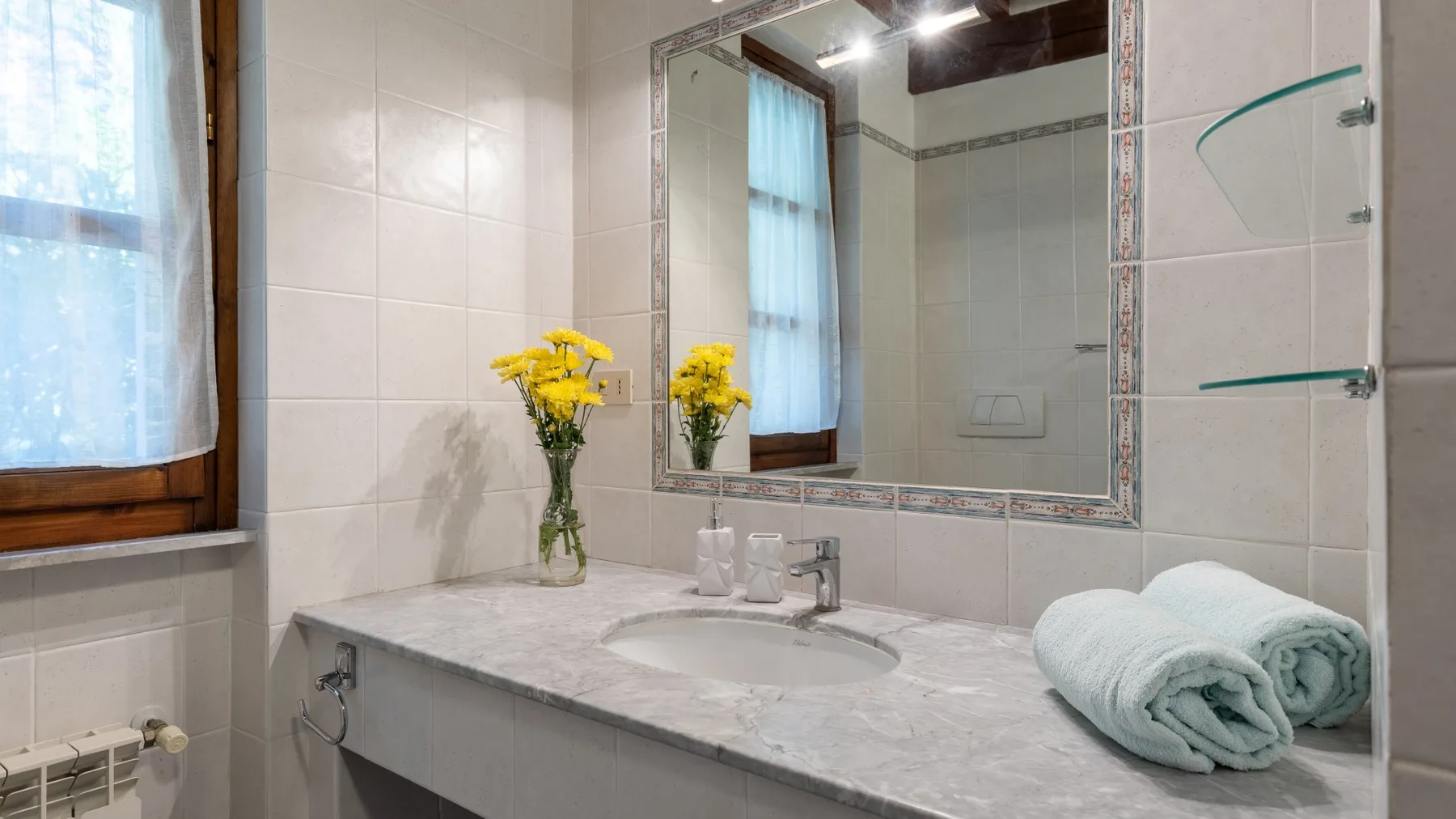Un tocador de baño con espejo, lavabo y toallas dobladas junto a una ventana.