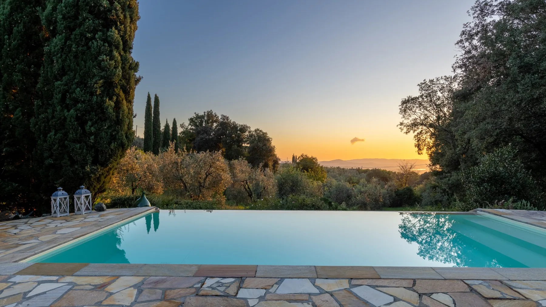 Una piscina al aire libre da a un paisaje arbolado al atardecer.