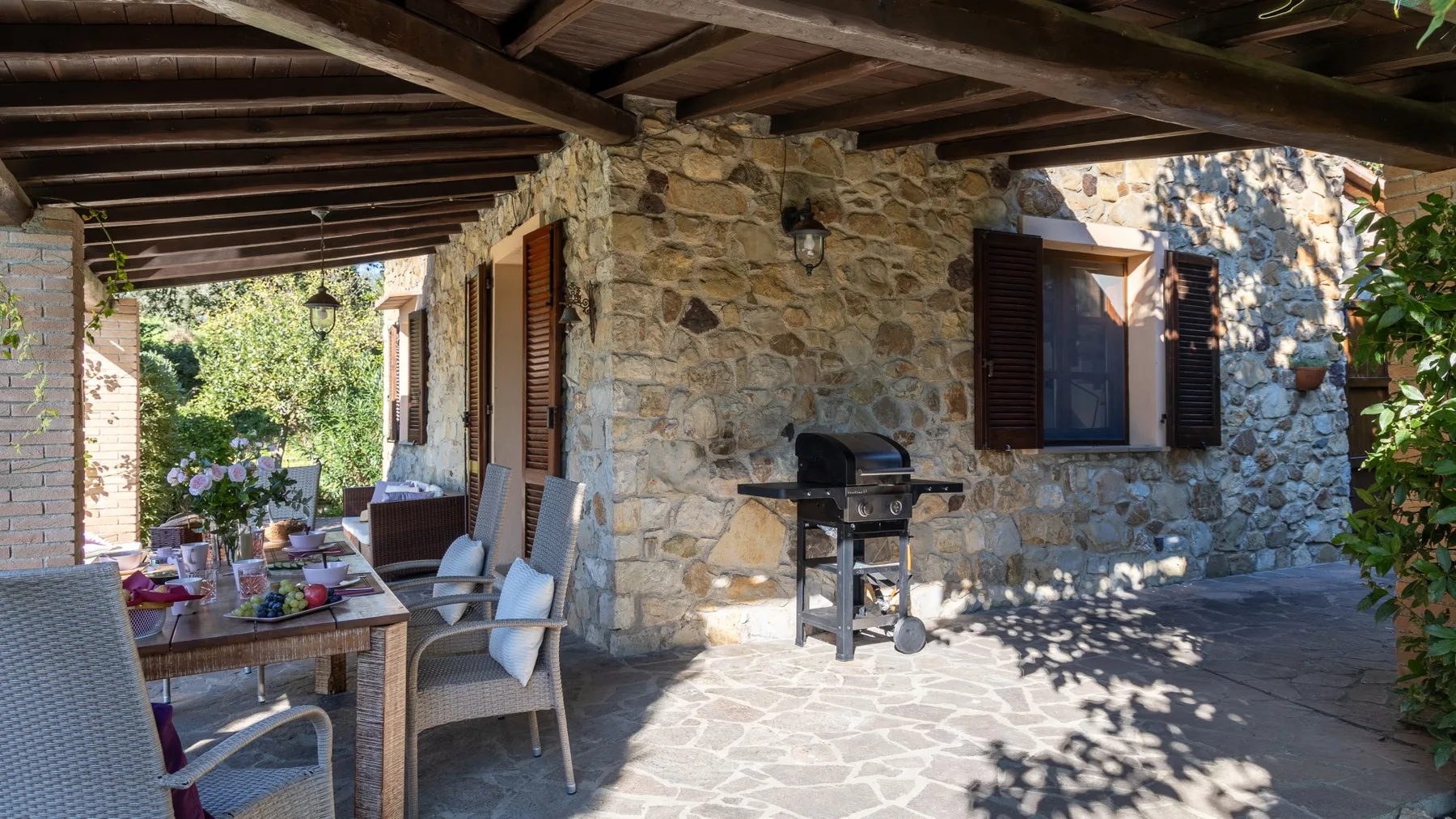 Un patio de piedra a la sombra, con asientos al aire libre y una parrilla.