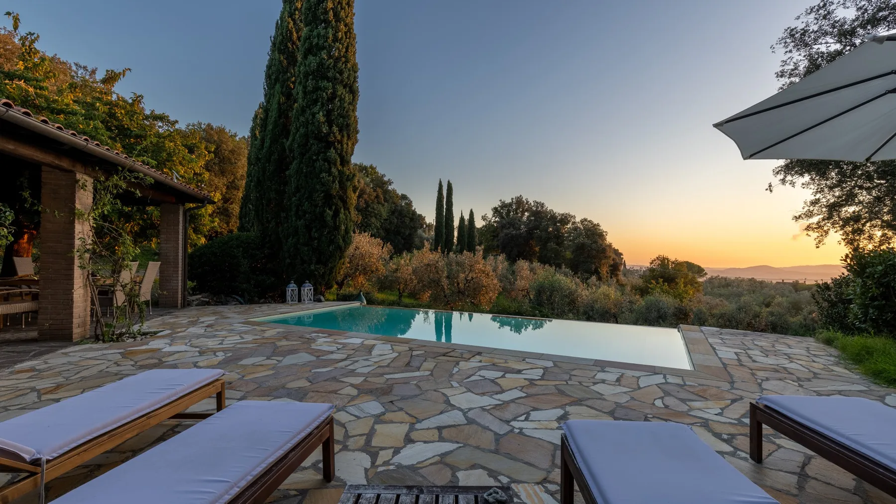 Un patio de piedra rodea una piscina con asientos reclinables y vistas al campo.