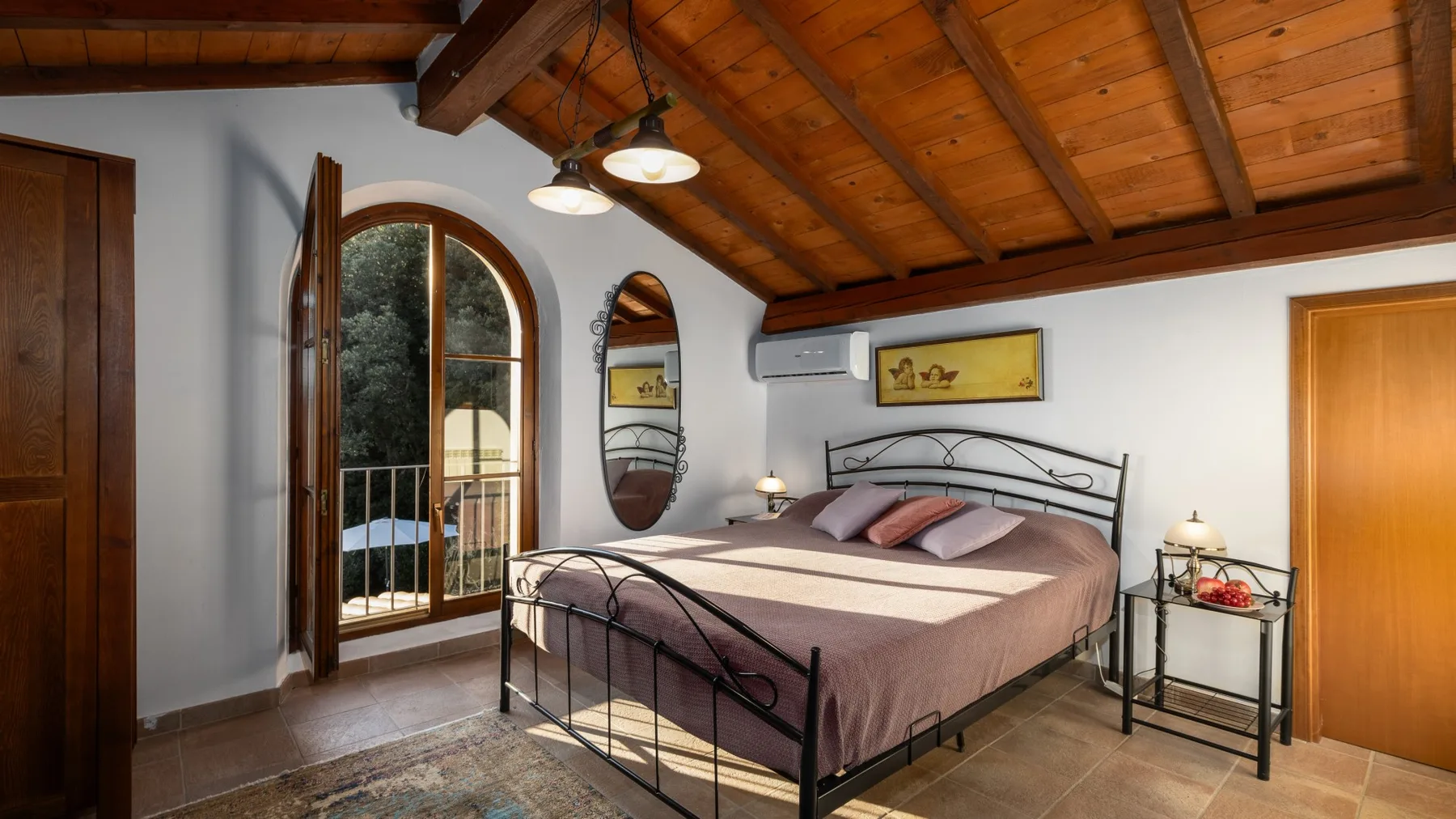 Un dormitorio con una cama de metal bajo un techo de madera y una puerta de vidrio arqueada.