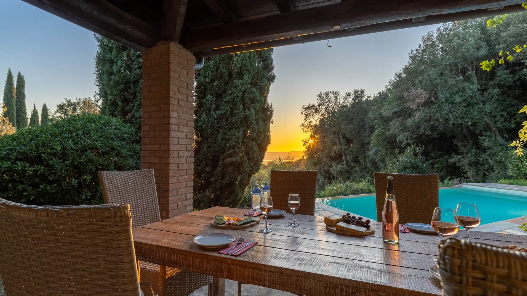 Una zona de comedor al aire libre cubierta da a una piscina y al atardecer.