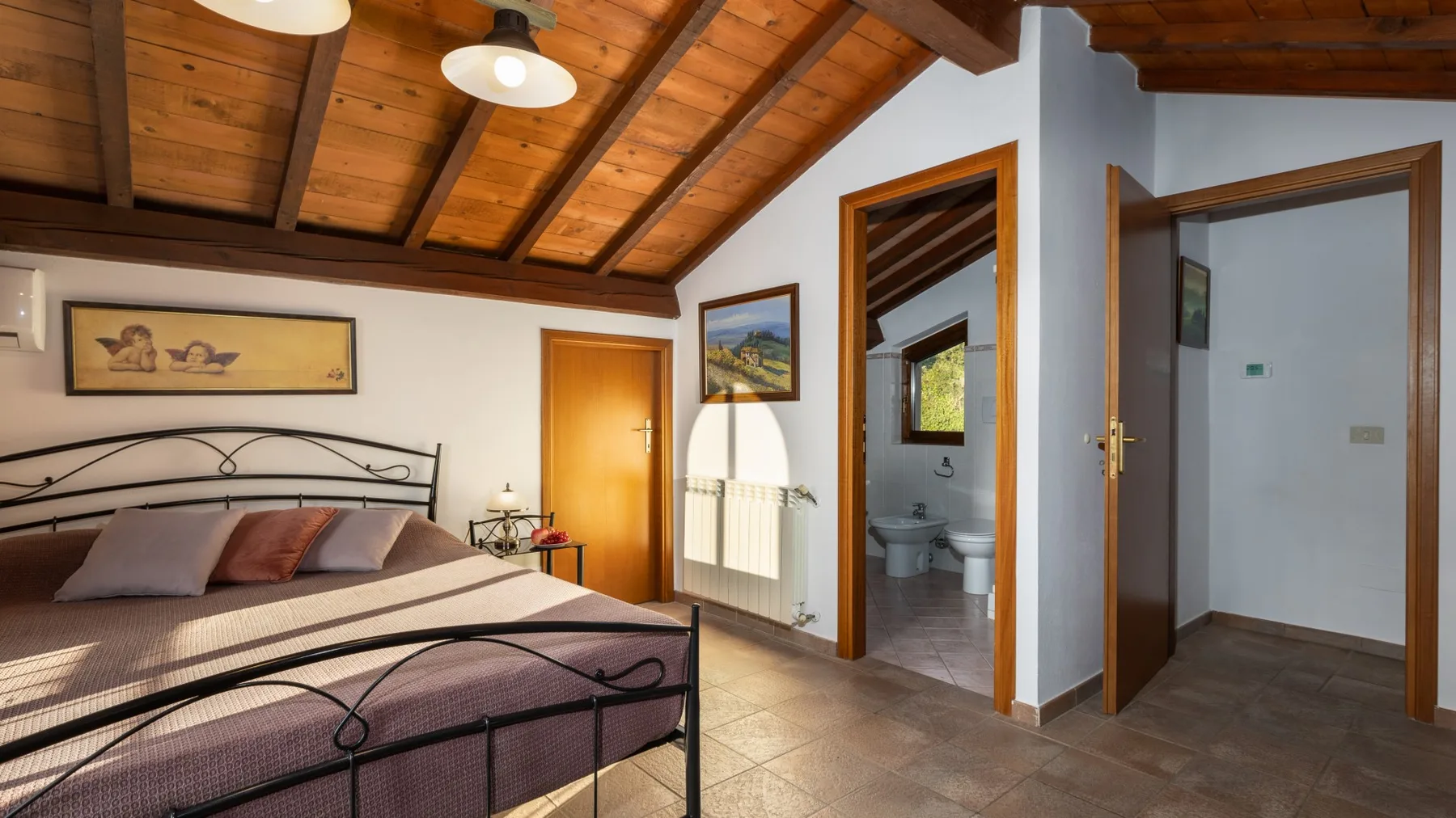 Un dormitorio con una cama de metal bajo un techo de madera y una puerta abierta.
