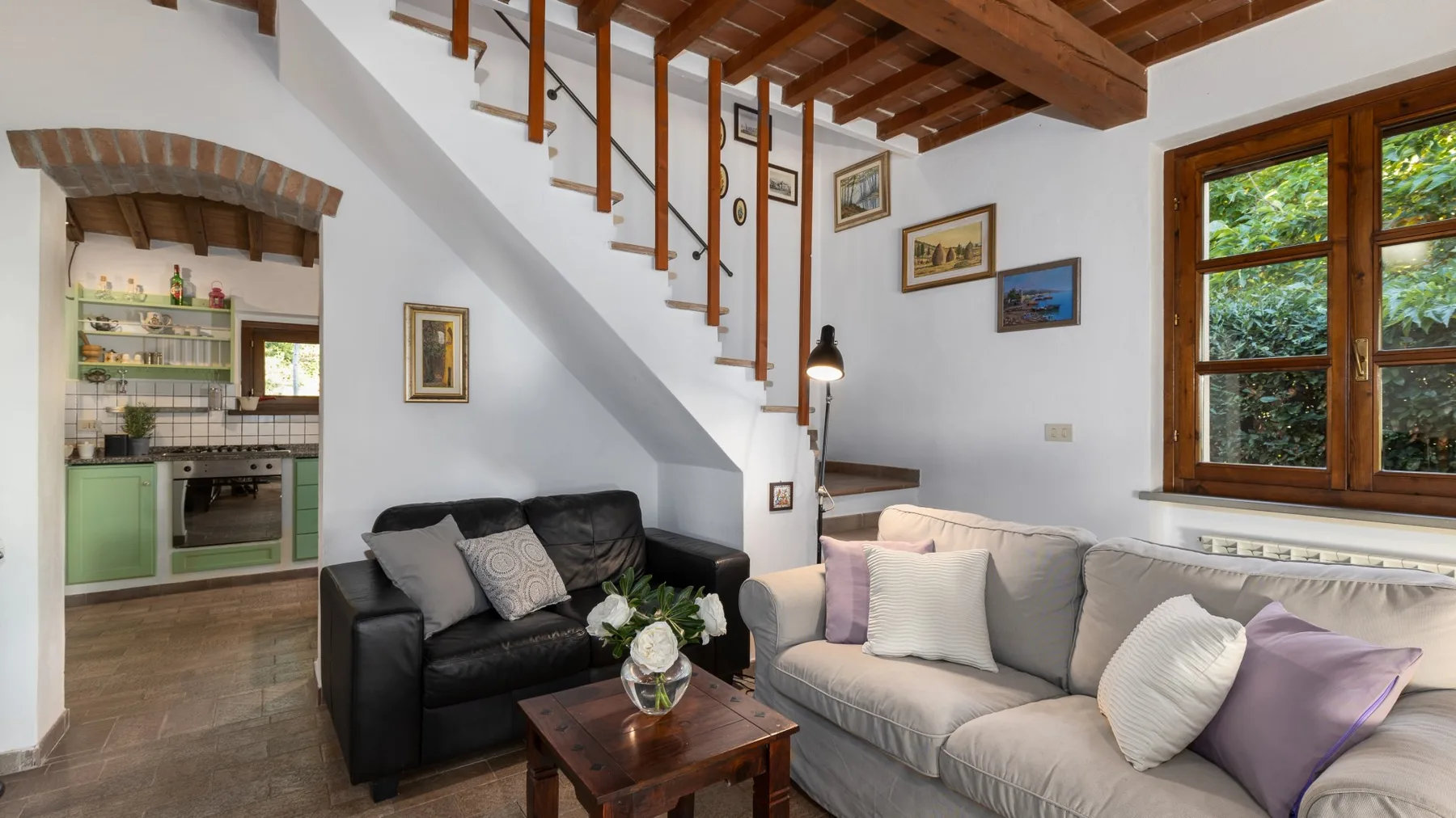 Una sala de estar con sofás bajo una escalera de madera y ventanas grandes.