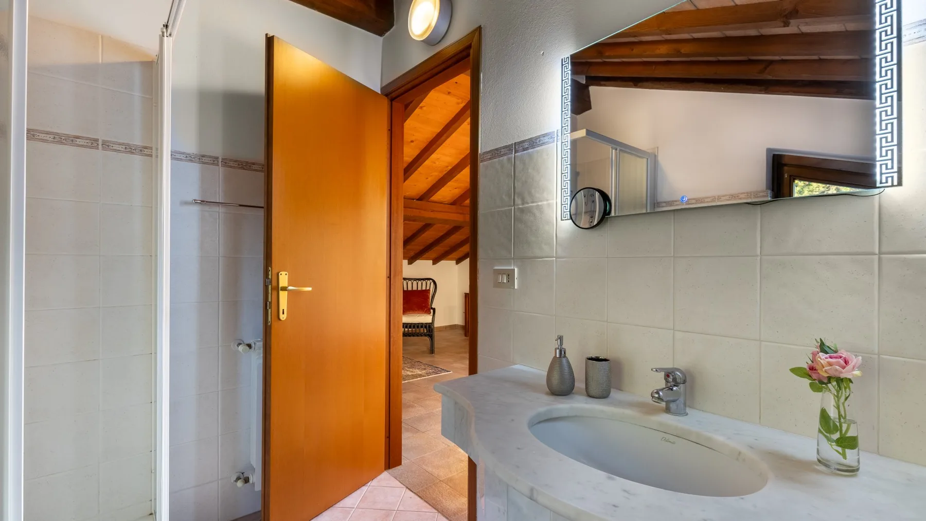 Un baño con azulejos, lavabo, espejo y puerta de madera abierta.