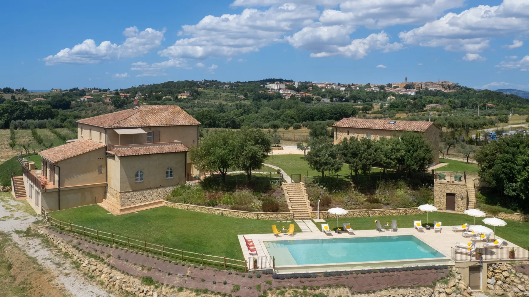 A swimming pool and landscaped grounds sit among buildings in a countryside setting.