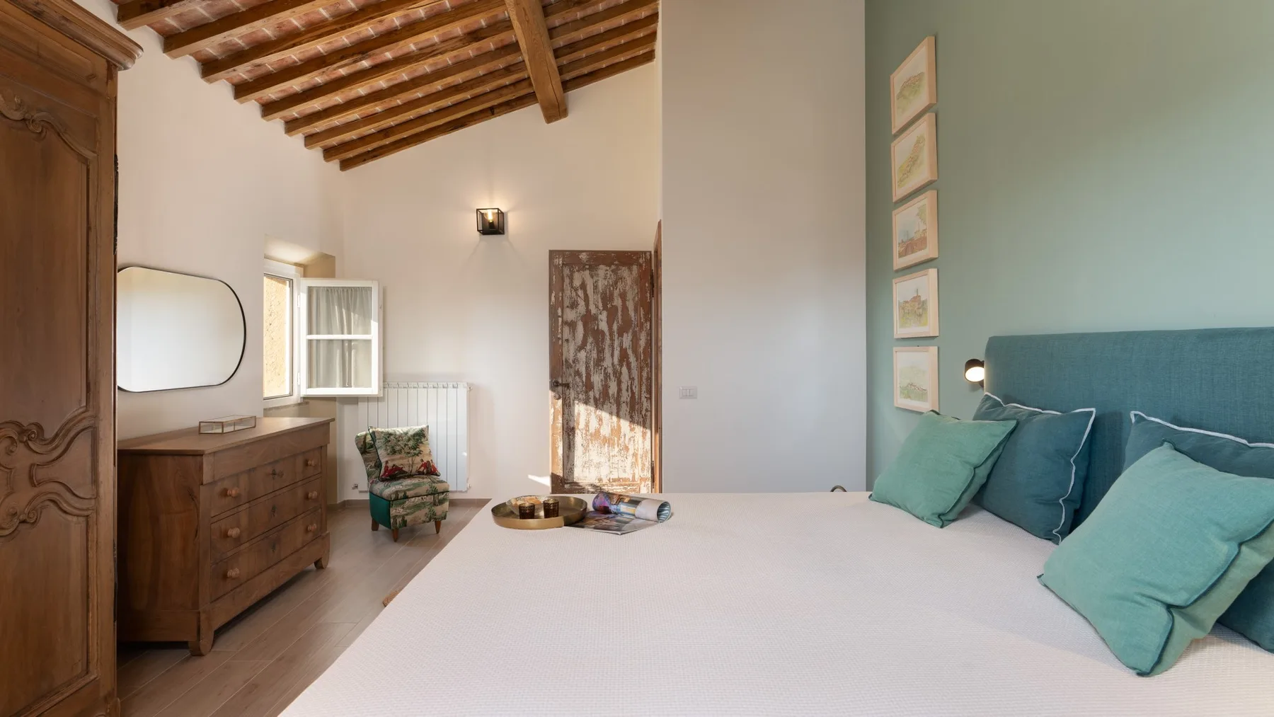 A bedroom with a large bed, wooden dresser, and exposed ceiling beams.