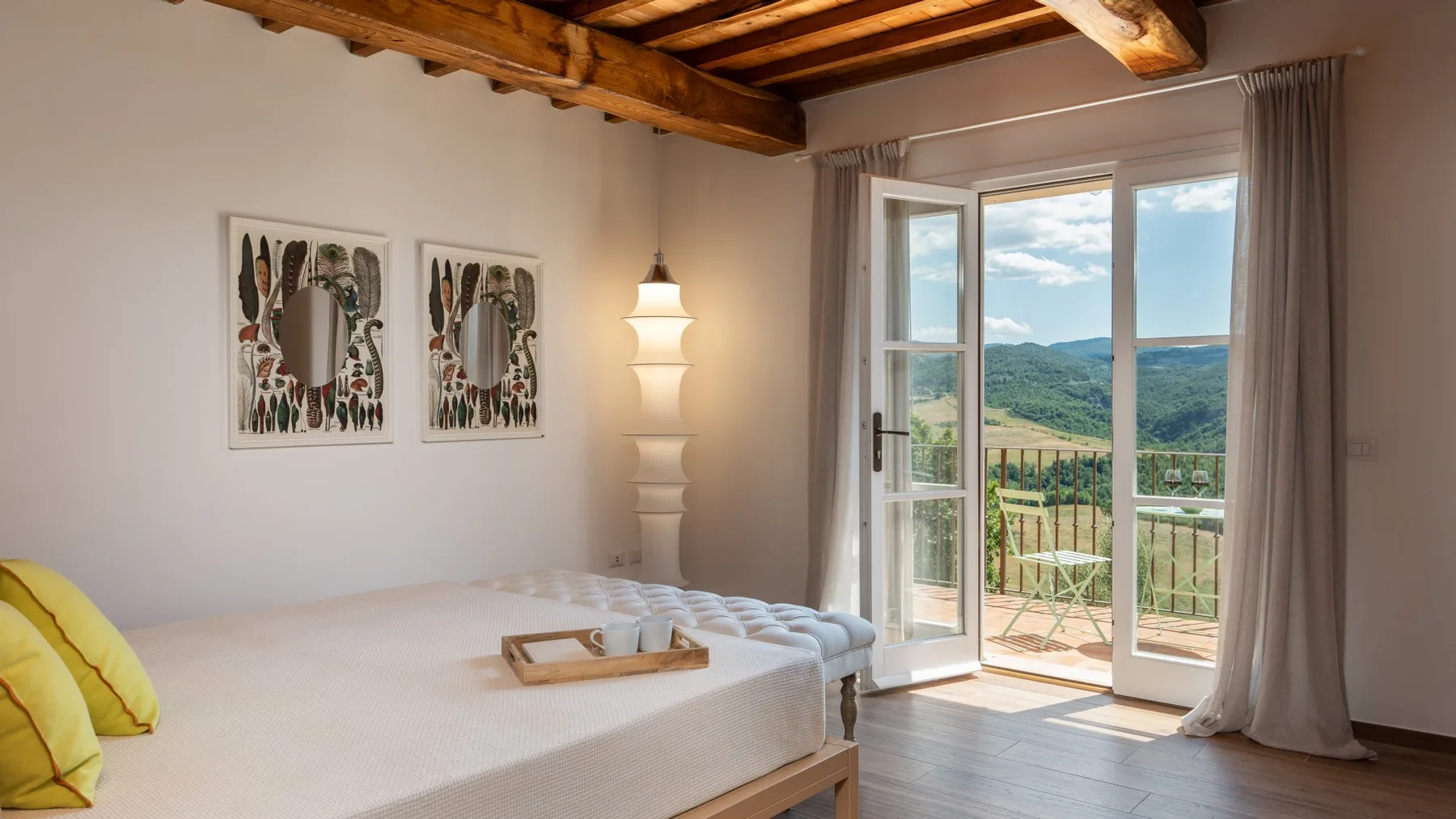 A bedroom with a bed beside open glass doors overlooking a green landscape.