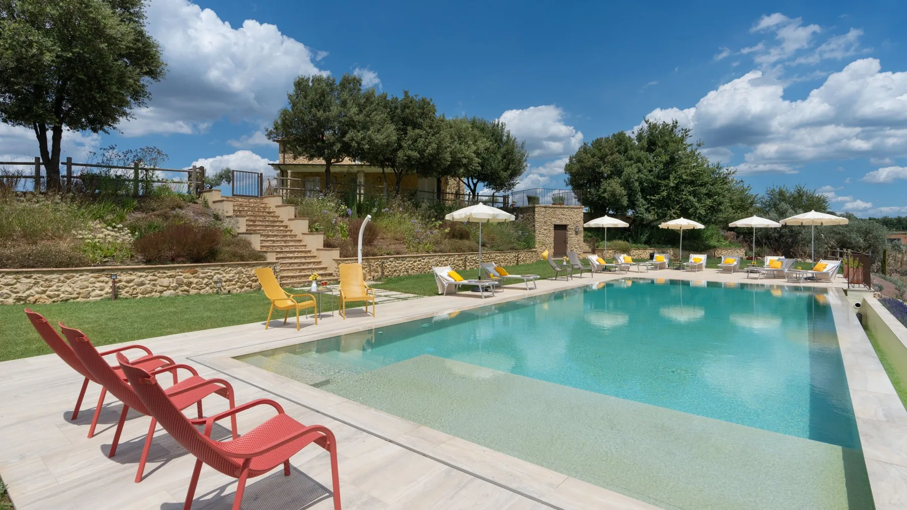 An outdoor swimming pool is surrounded by lounge seating and umbrellas.