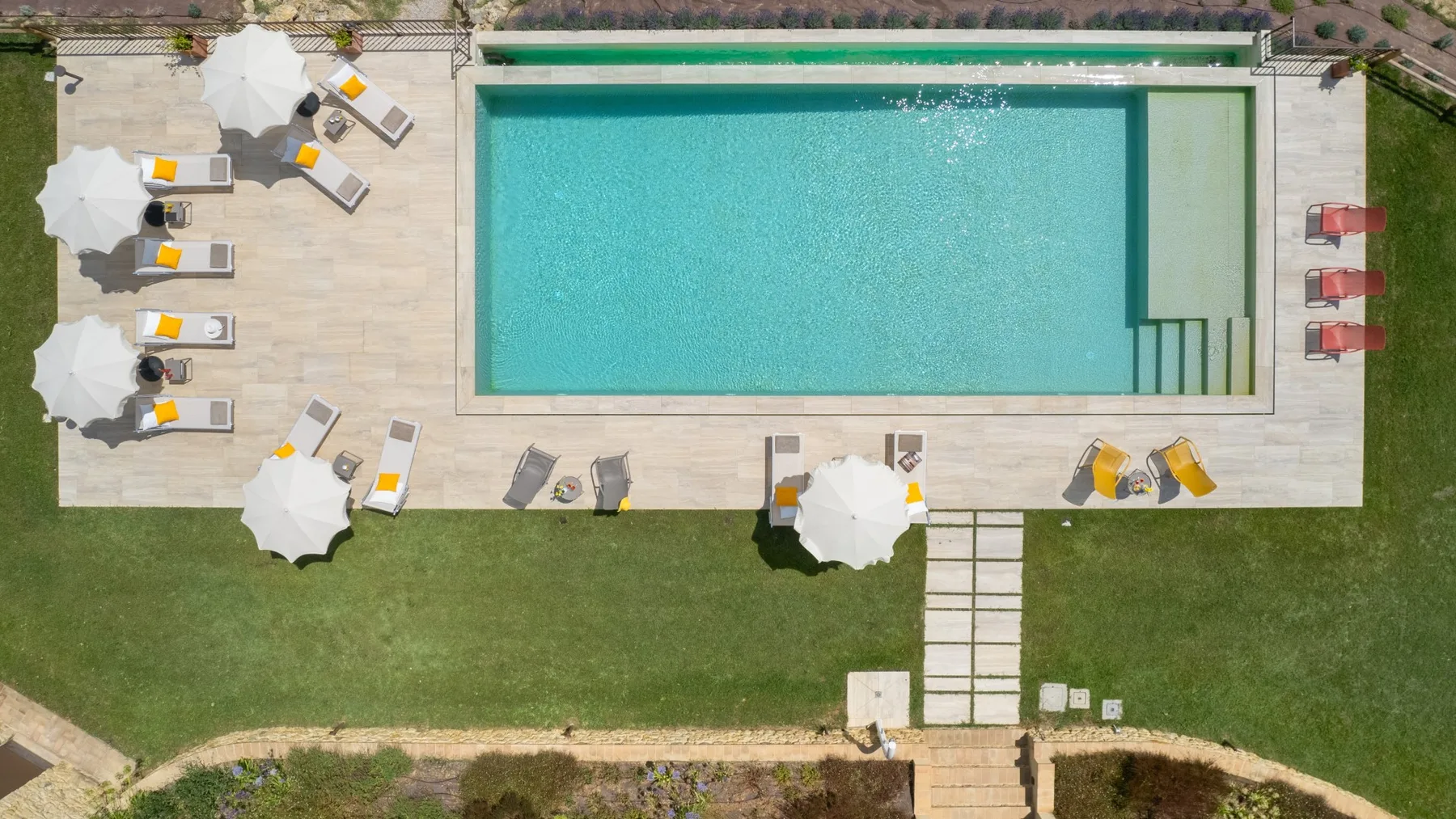 An outdoor swimming pool is surrounded by a paved deck and lawn.