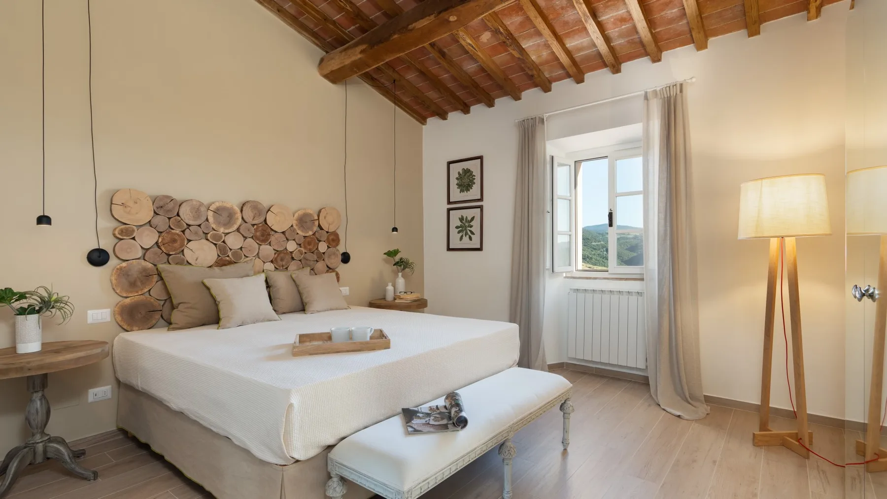 A bedroom with a large bed, a bench, and a window beneath exposed wooden beams.