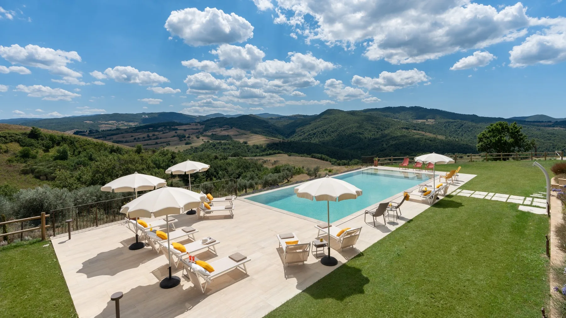 An outdoor pool and sun deck overlook rolling green hills beneath a partly cloudy sky.