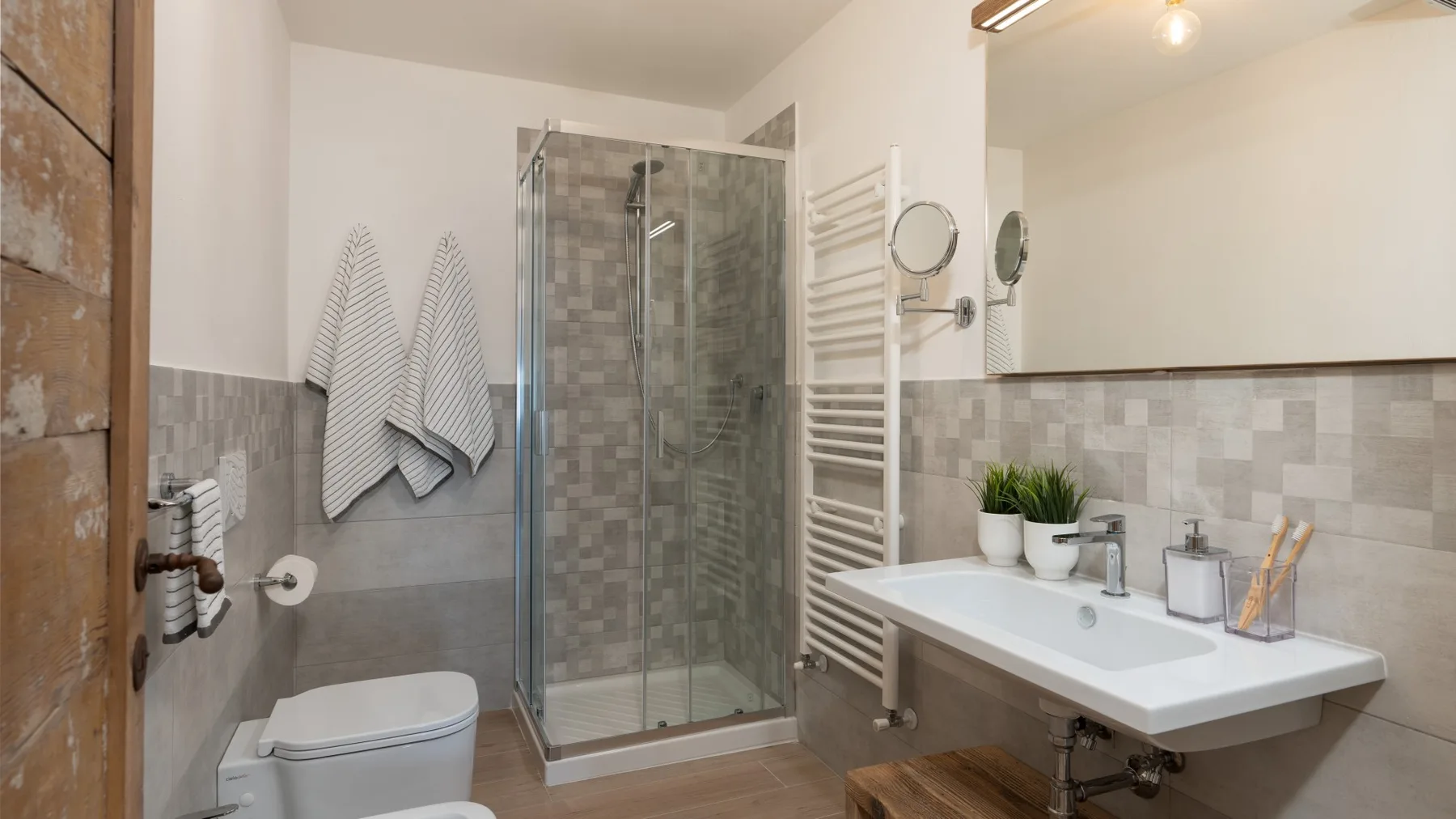 A tiled bathroom with a glass shower, toilet, and wall-mounted sink.