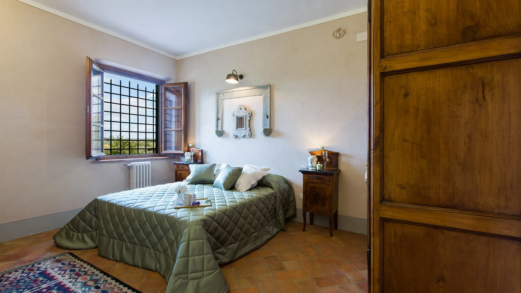 A bedroom with a double bed, a window, and a small bedside table.