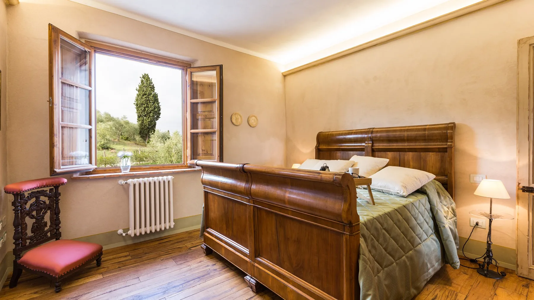 A bedroom with a wooden bed and an open window overlooking greenery.