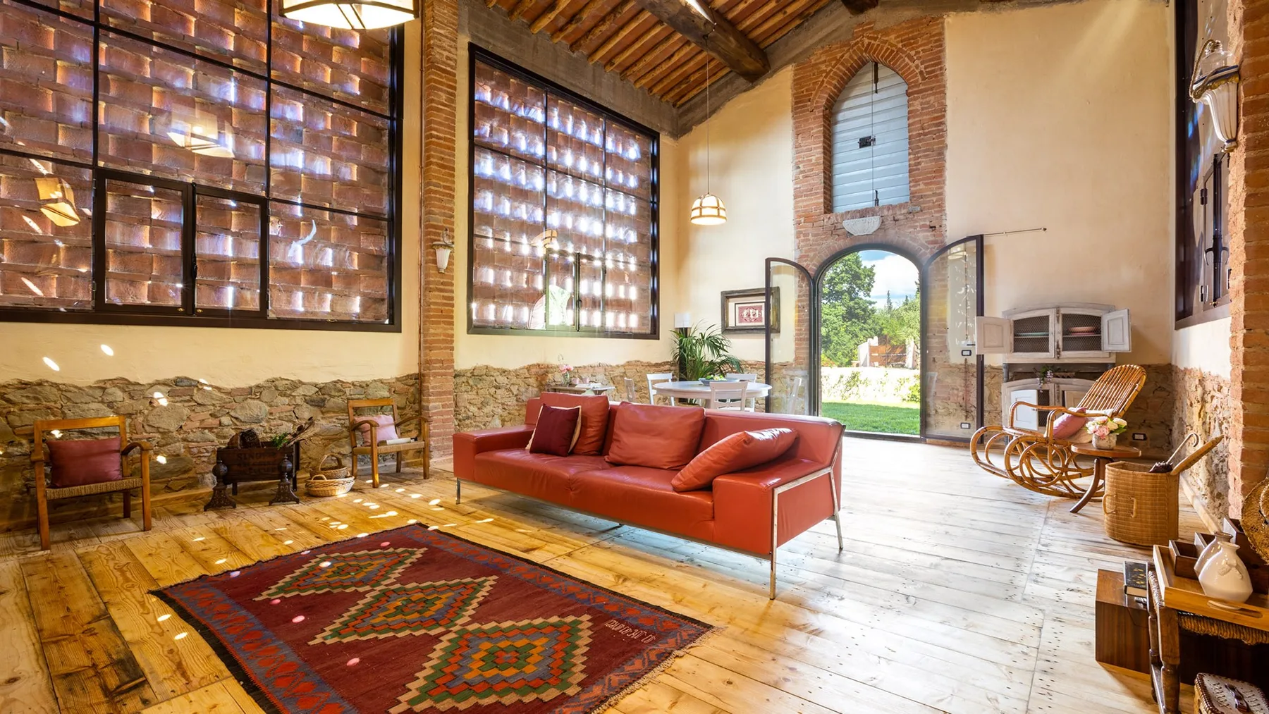 A rustic living room with red seating, large windows, and an open arched doorway.