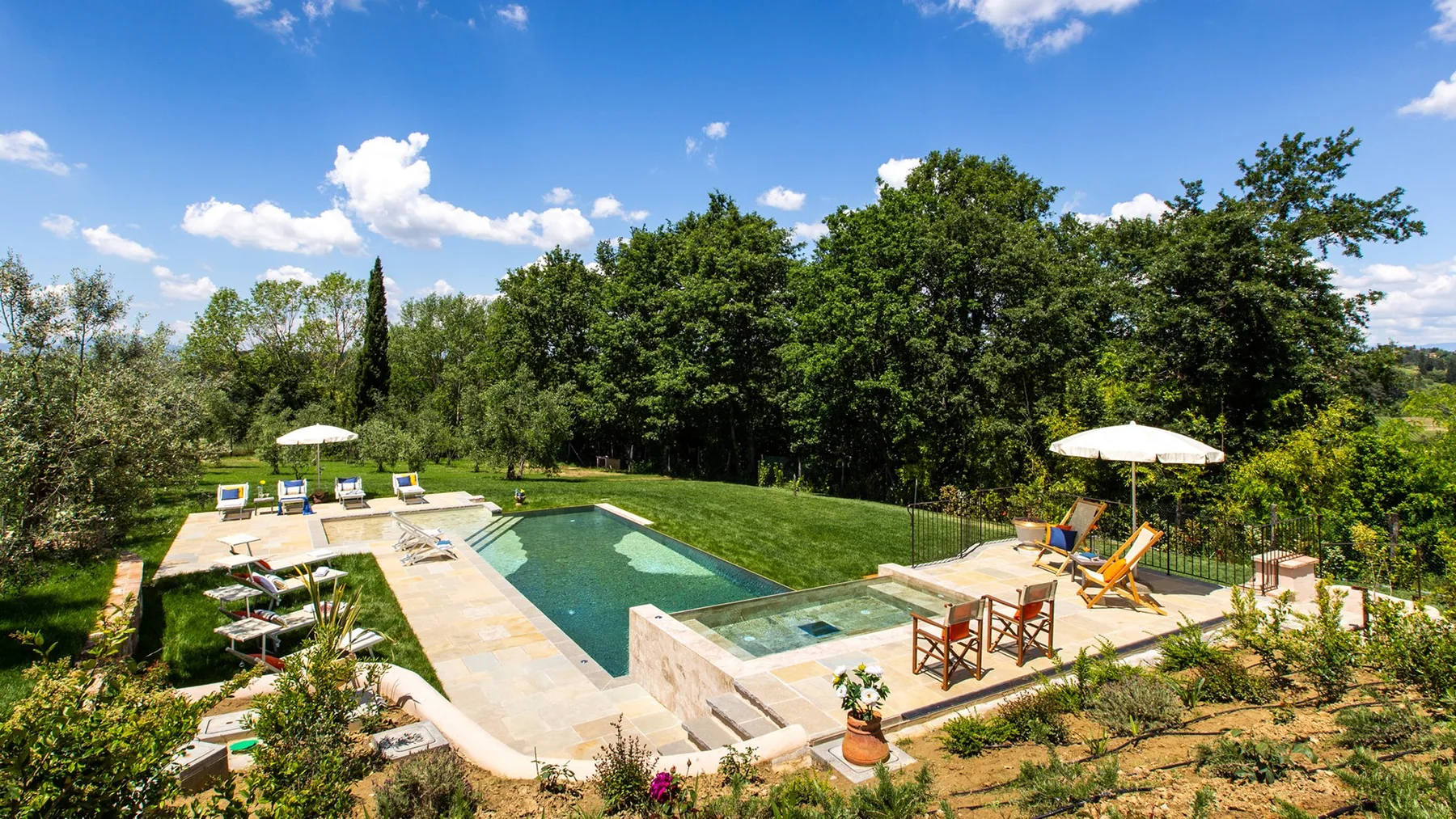 An outdoor swimming pool sits beside a lawn, with lounge seating and umbrellas.