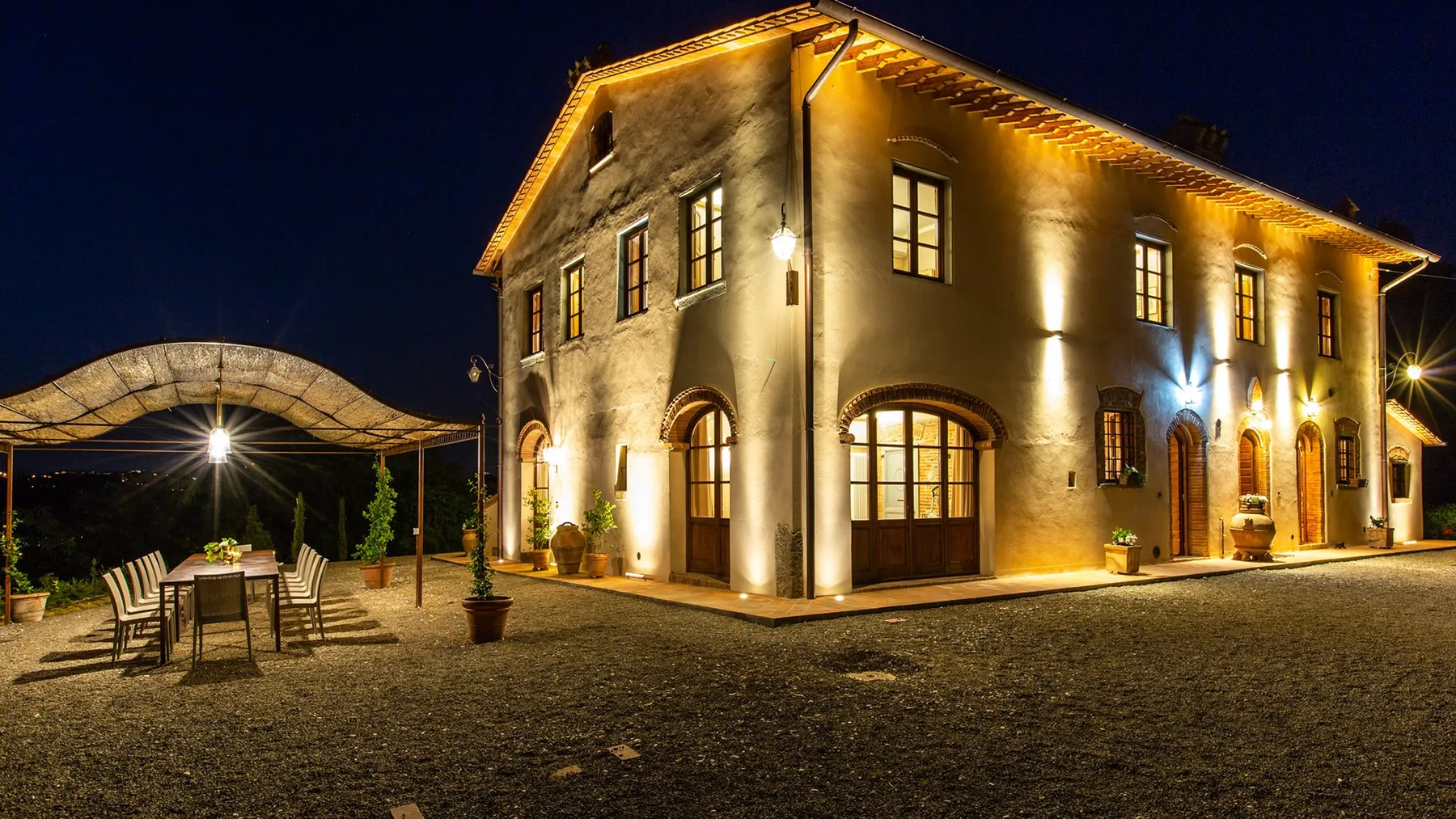 A warmly lit building stands beside an outdoor dining area at night.