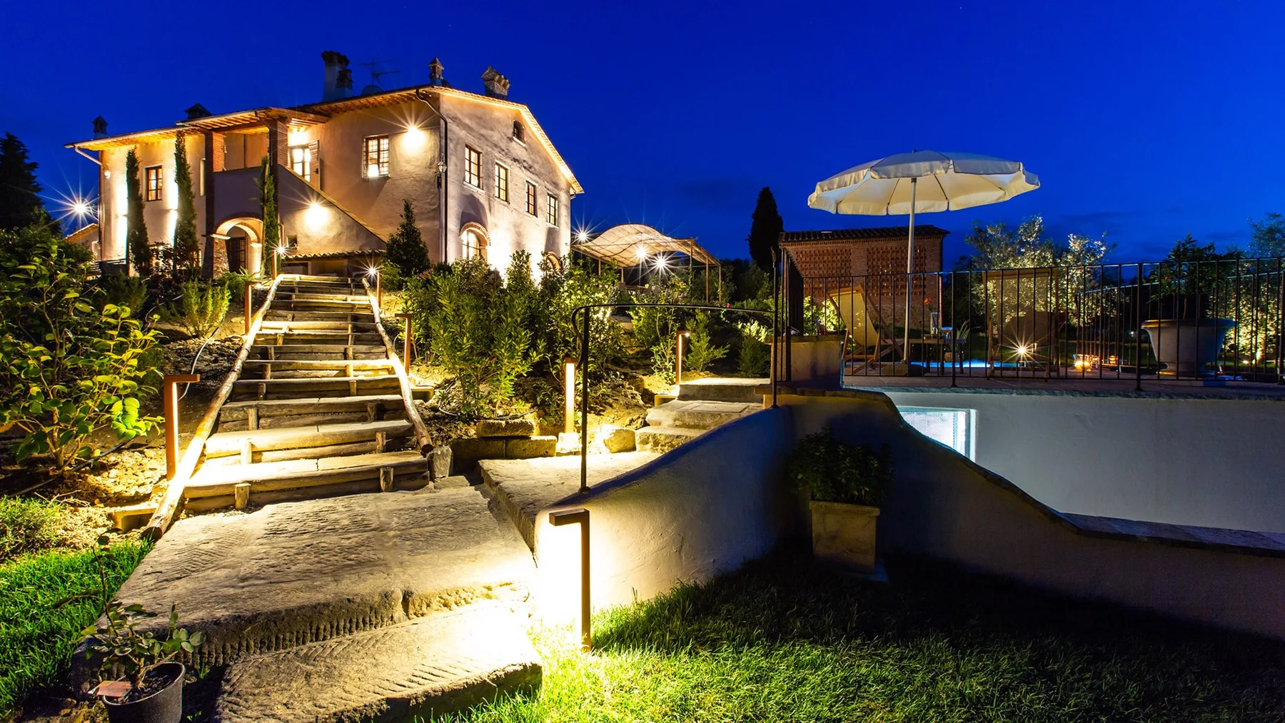 An illuminated house and landscaped garden with steps under a deep blue evening sky.