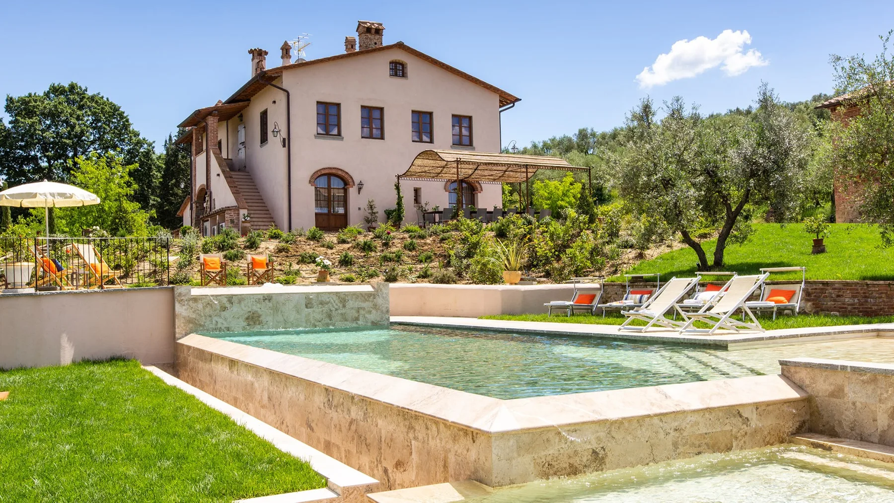 A house overlooks a raised swimming pool surrounded by garden seating.